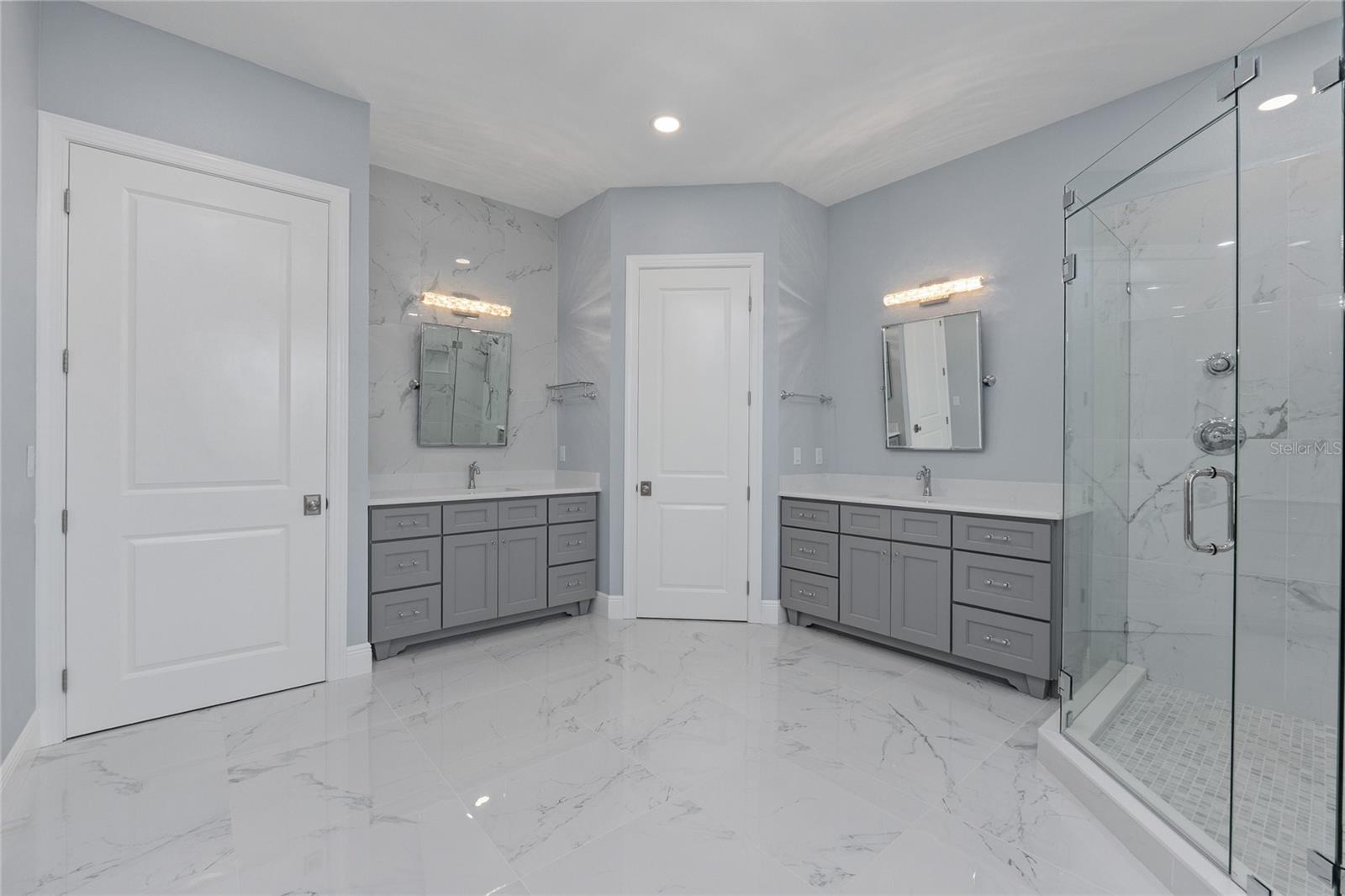 Dual vanities with a water closet and linen closet.  Large format tile graces the floor and walls and quartz on the countertops