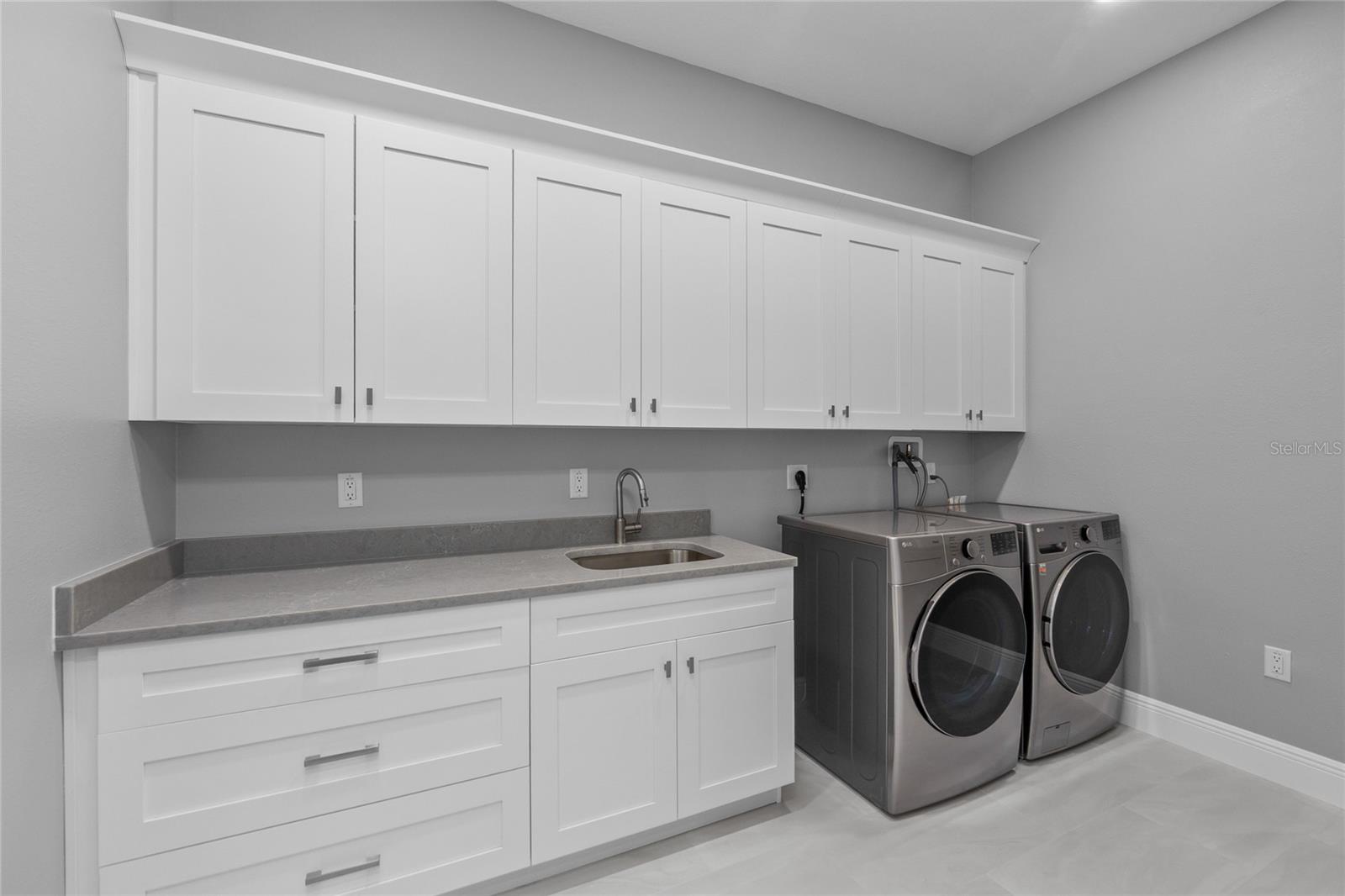 Spacious Laundry Room with front loading washer and dryer, cabinets for storage and quartz countertops