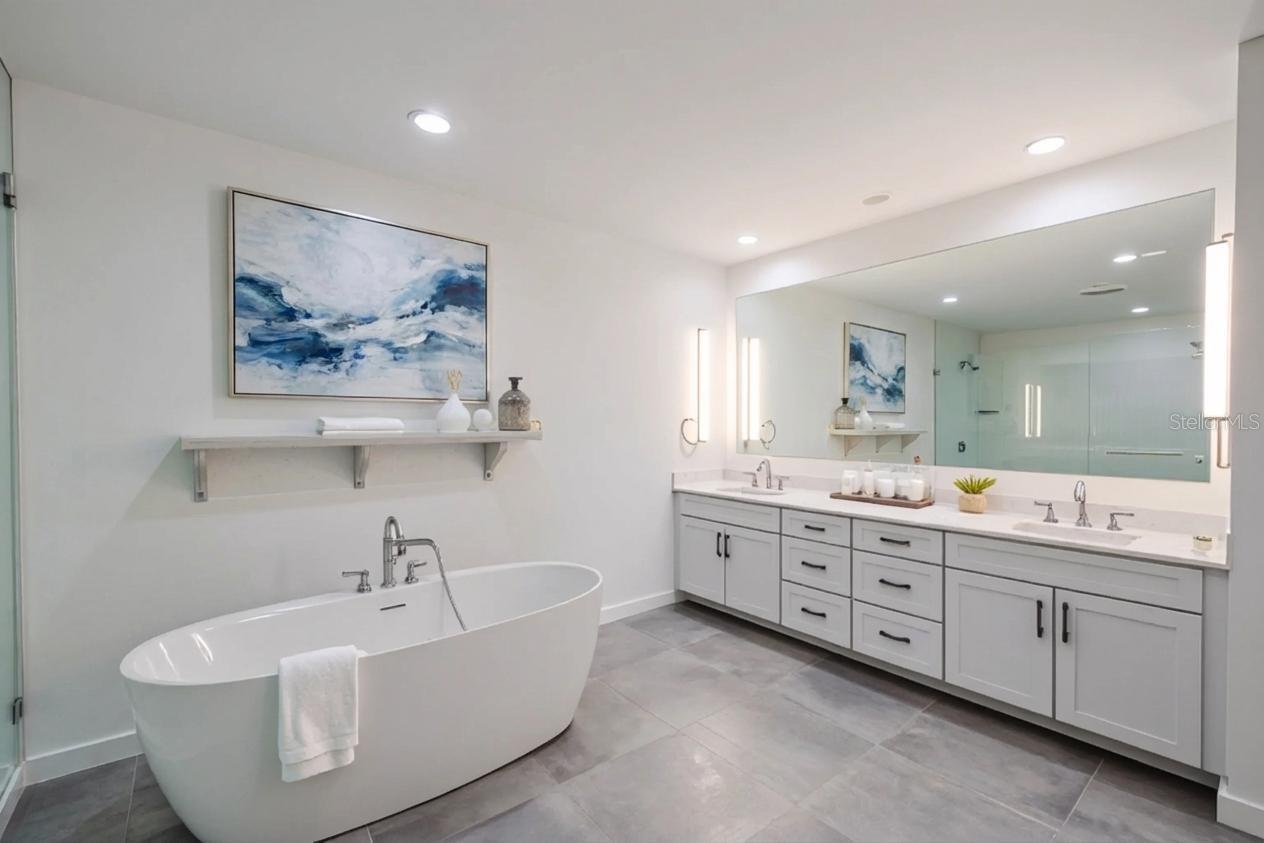 The primary bathroom features a sophisticated double vanity with an expansive quartz countertop, dual undermount sinks, and abundant drawer storage. Sleek brushed nickel hardware and soft-close cabinetry complement the clean, modern aesthetic. A full-width mirror framed by contemporary vertical sconces provides excellent lighting and adds to the spa-like ambiance of this beautifully designed space.