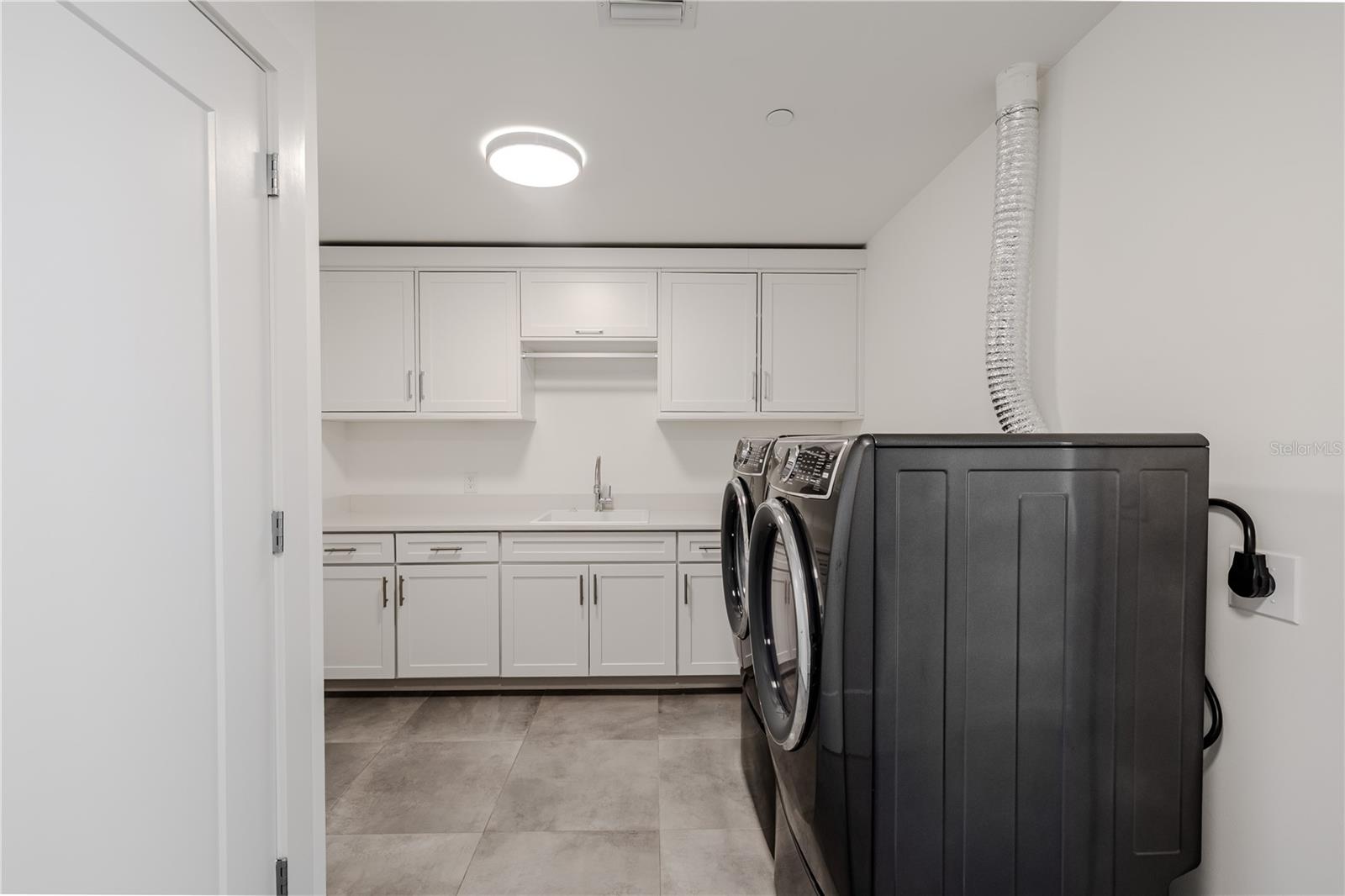 This spacious, well-appointed laundry room combines function and style with sleek cabinetry, quartz countertops, and abundant storage. A deep sink and full-size front-loading washer and dryer make laundry tasks effortless.