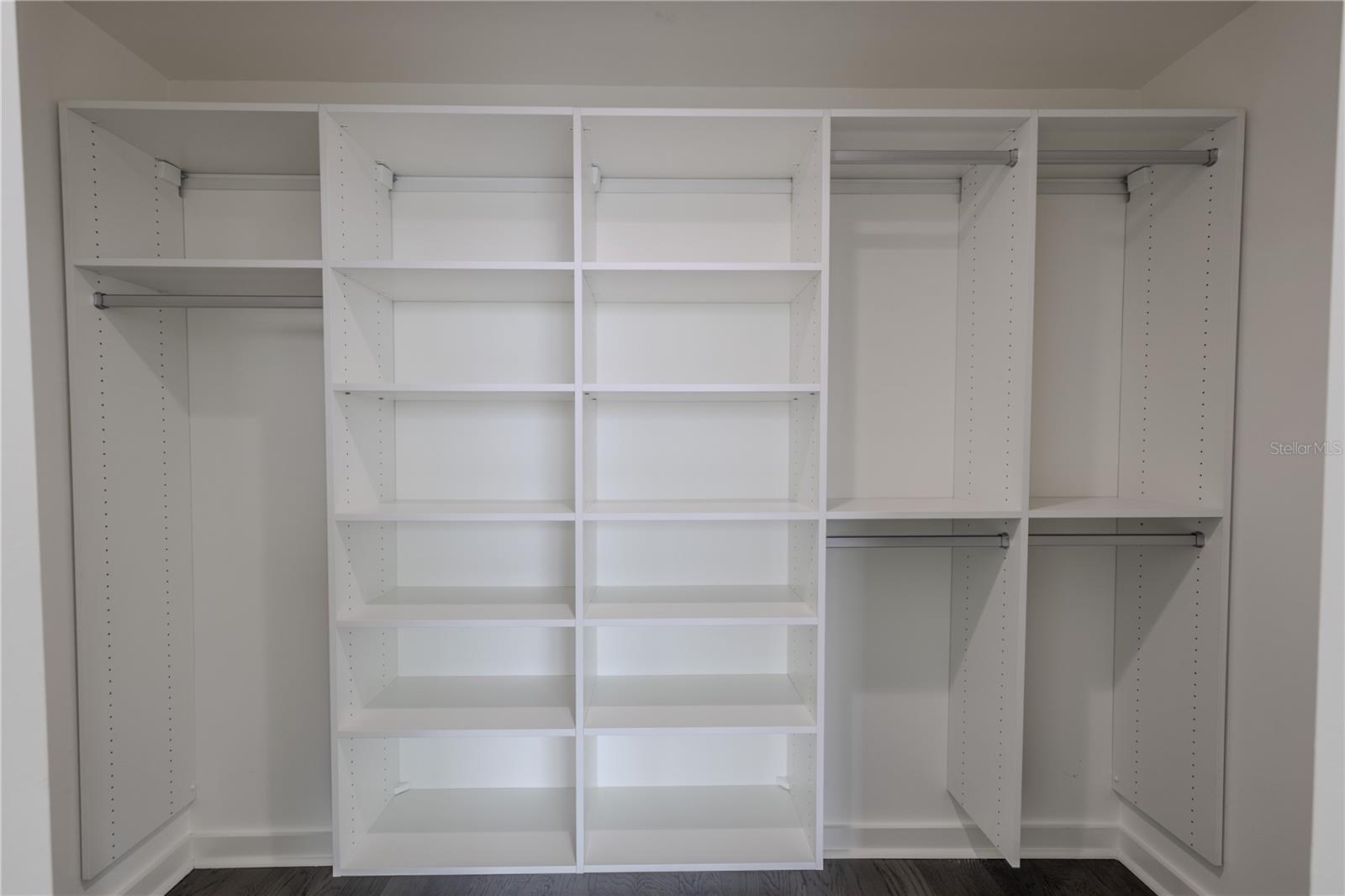 The spacious walk-in closet for Bedroom 2 offers exceptional organization with a custom built-in system featuring multiple open shelves and double hanging sections. Clean white finishes and adjustable shelving provide versatility for clothing, shoes, and accessories, while the streamlined layout maximizes storage and accessibility. Perfectly designed to complement the modern style of the suite, this closet delivers both form and function in a bright, polished space.