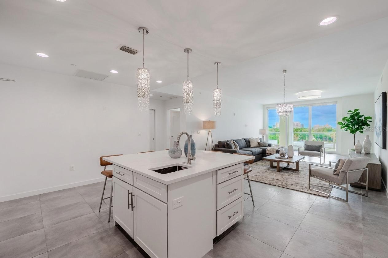 From the kitchen, enjoy an open-concept view that seamlessly connects the dining and living areas. Sleek tile flooring and designer lighting create a bright, contemporary flow, while floor-to-ceiling sliding glass doors frame lush treetop and skyline views beyond the spacious balcony