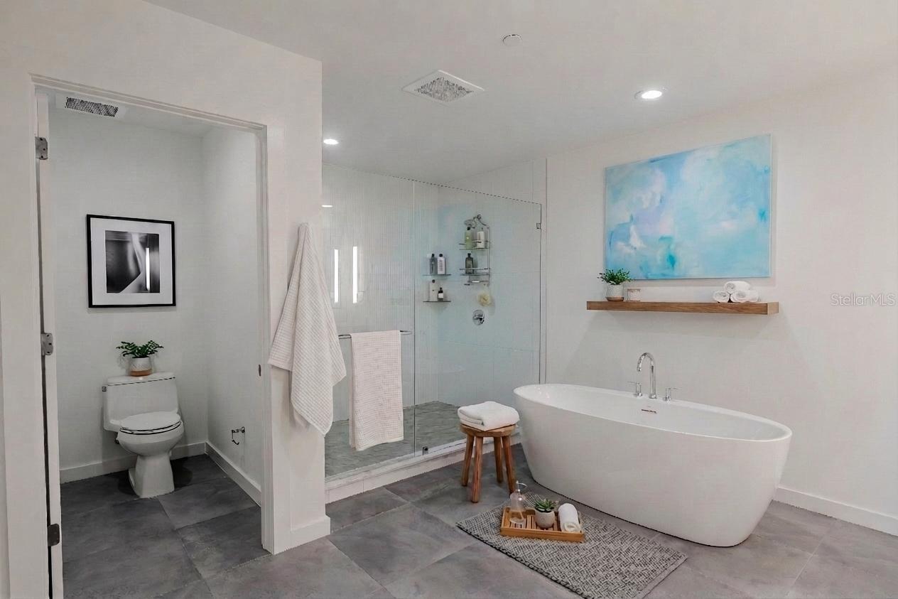 The luxurious primary bathroom exudes spa-like serenity with a sleek, modern design. A private water closet, a freestanding soaking tub serves as the elegant focal point, complemented by a frameless glass-enclosed walk-in shower