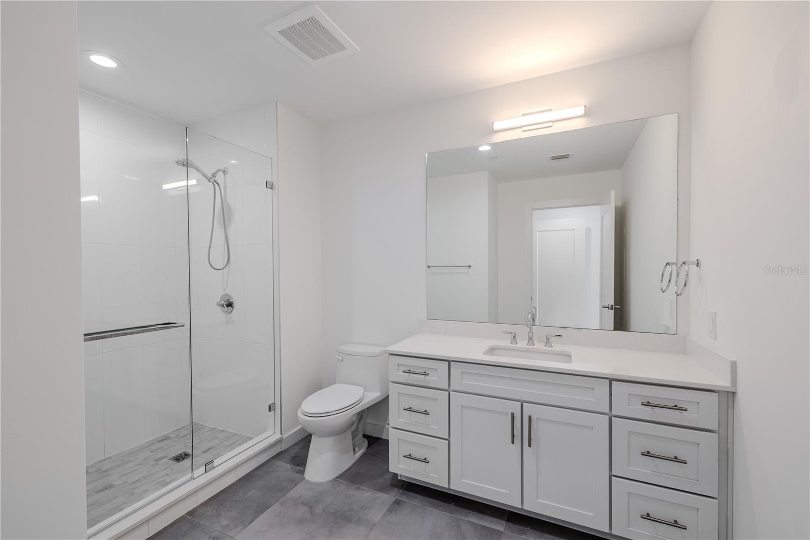 3rd bathroom Ensuite: The single vanity features shaker-style cabinetry with brushed nickel hardware, a sleek quartz countertop, and an oversized mirror with contemporary lighting above. Thoughtfully designed for both comfort and style, this ensuite combines modern elegance with everyday functionality — a private, polished extension of Bedroom 3.