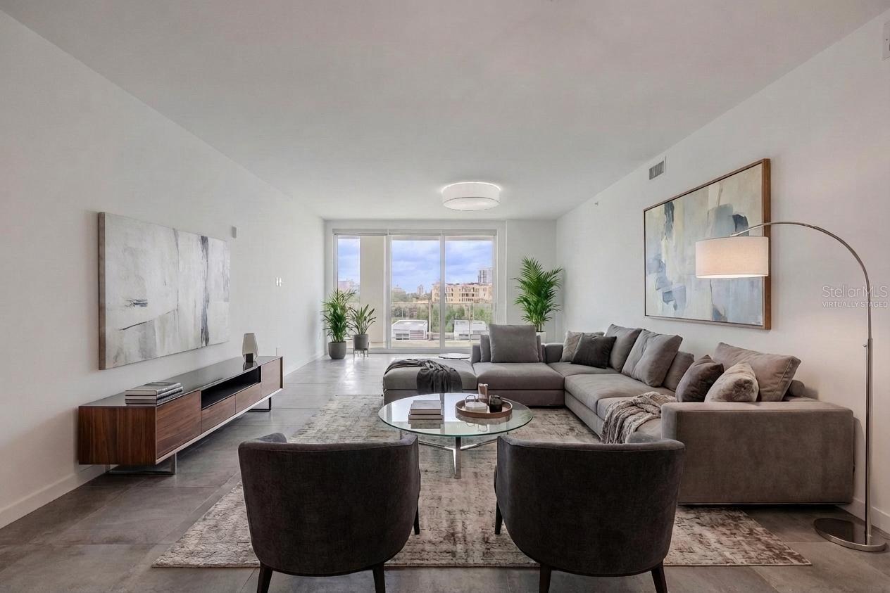 This bright and spacious dining and living area offers an elegant, open layout with sleek tile flooring and contemporary lighting. Floor-to-ceiling glass doors flood the space with natural light and open to a large balcony with sweeping water and skyline views. The modern chandelier adds a touch of sophistication, creating the perfect setting for entertaining or relaxing in style. Virtually staged photo.