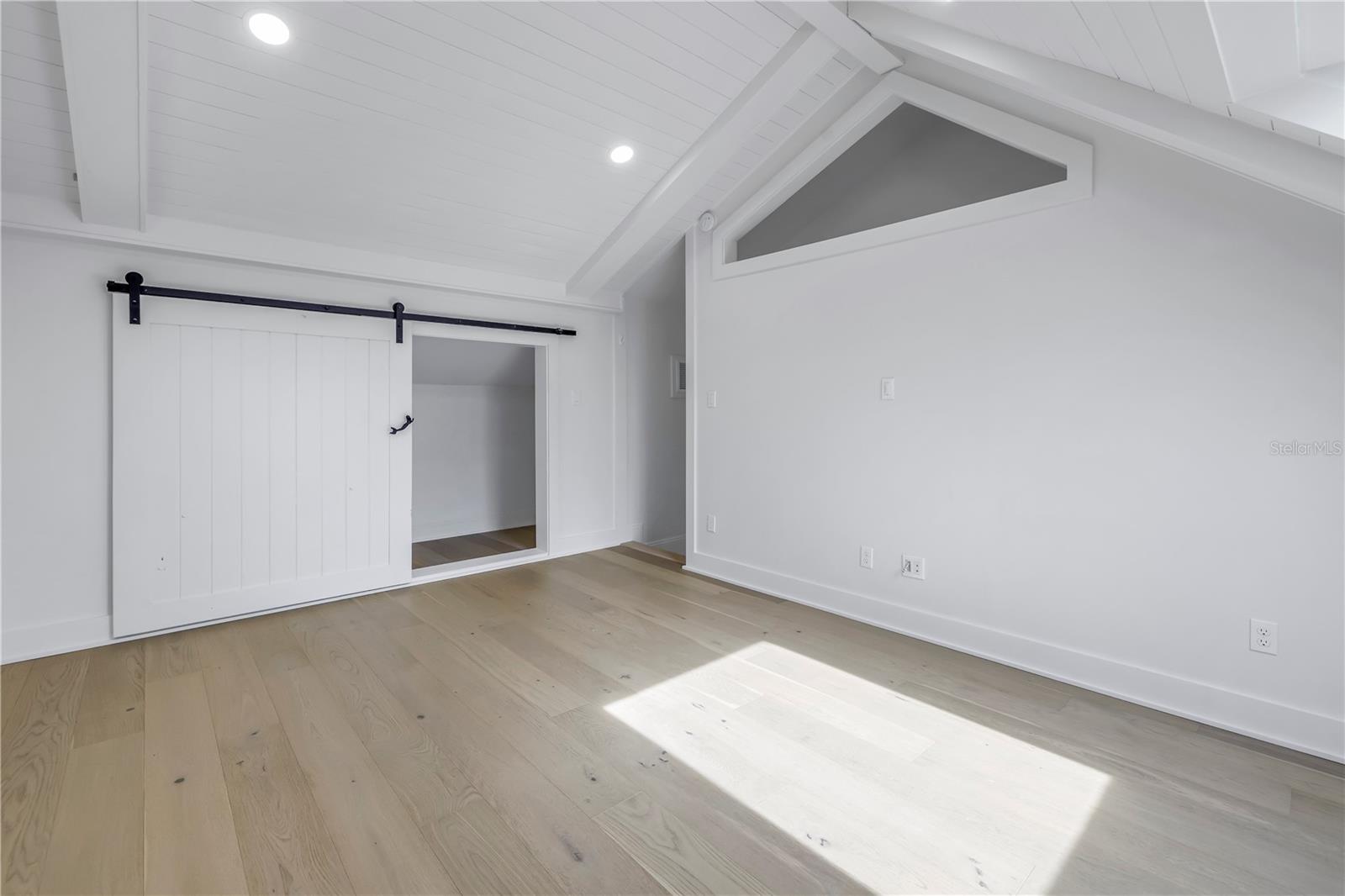 Upstairs bedroom with barn door closet and high ceiling, engineered wood flooring