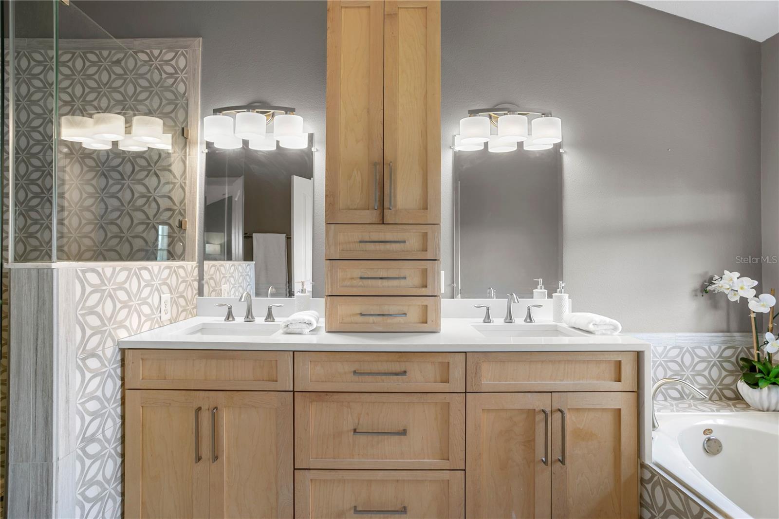 A spa-inspired bathwith dual vanities, light wood cabinetry, and a soaking tub.