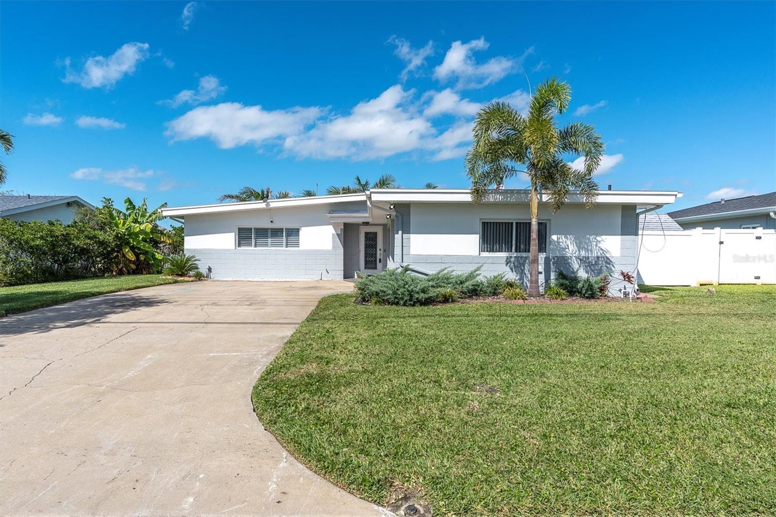 Front view of the home showcasing its classic Floridian design, sturdy block and stucco build, and spacious front yard with palms.