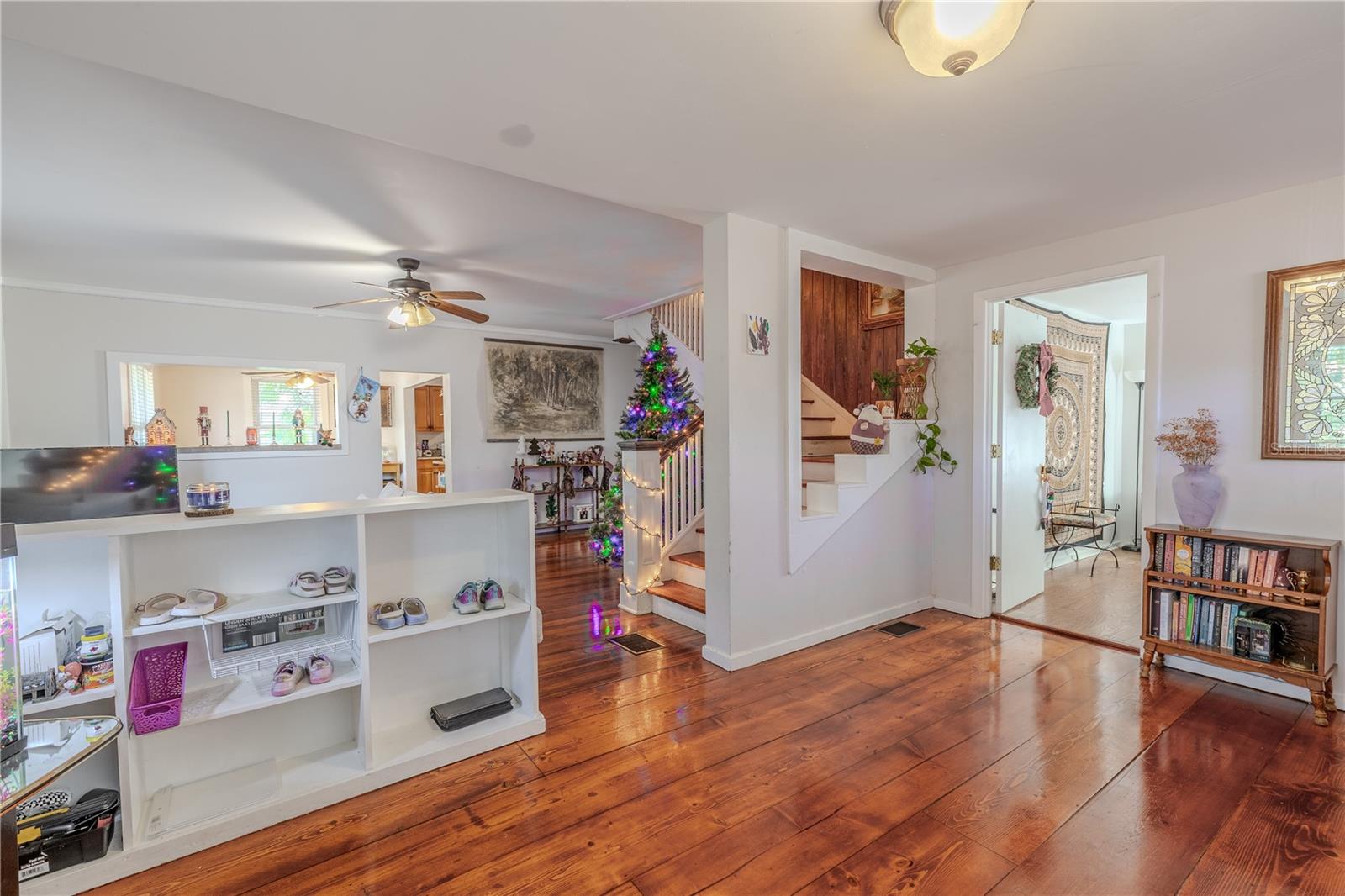 From the foyer, this view highlights the home’s flowing layout and functional design. To the right, the entrance to a versatile bonus room offers additional space perfect for an office, playroom, or hobby area. Just beyond the half wall on the left is the main living room, creating an open feel while still defining each area. To the right, the staircase leads to the second floor, showcasing the home’s classic two-story layout. Abundant natural light and warm wood floors continue throughout, enhancing the inviting atmosphere of this historic home.