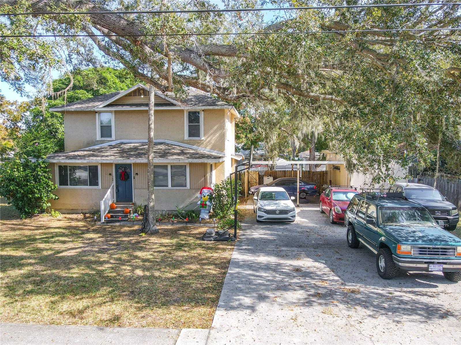 This front-facing view showcases the full charm and functionality of this 1918 historic home. Mature oaks arc gracefully overhead, creating a picturesque canopy above the spacious front yard and welcoming entryway. To the right, the expansive driveway offers exceptional parking capacity—ideal for multiple vehicles, guests, or recreational equipment—and leads directly to the covered carport and attached workshop. The home’s classic two-story structure, accented by large windows and thoughtful seasonal touches, creates a warm, inviting presence. This perspective beautifully highlights the property’s rare combination of character, ample outdoor space, and practical everyday convenience.