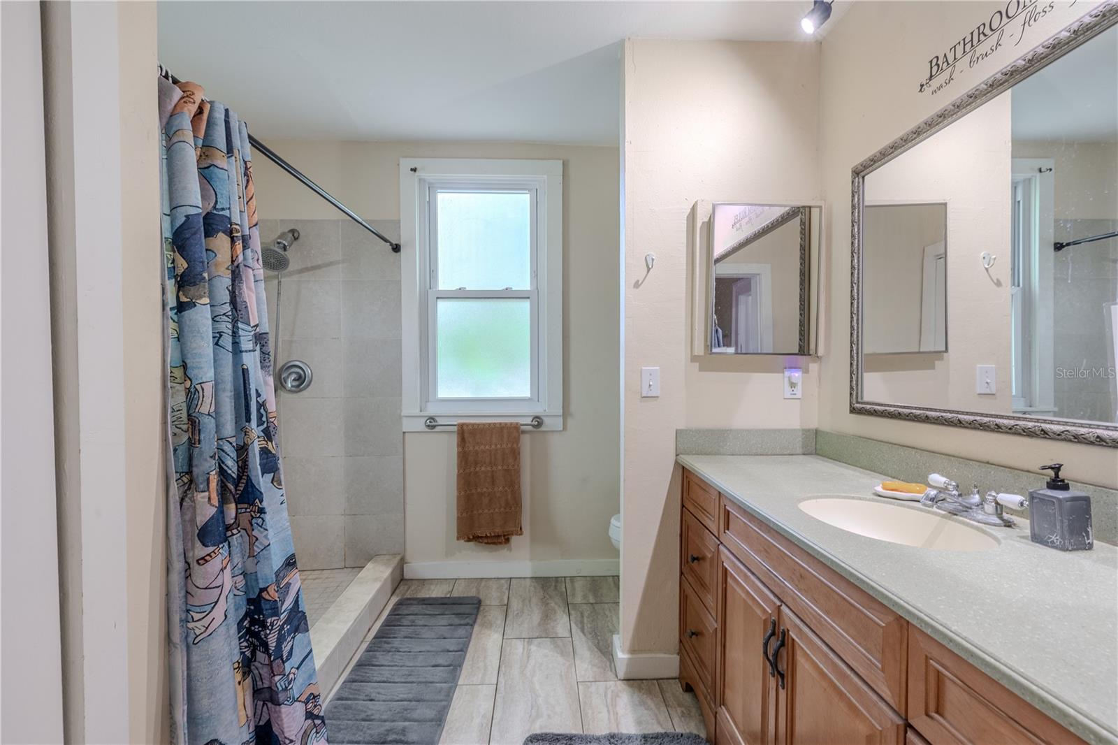 This spacious second-floor bathroom features a large walk-in shower, build in medicine cabinet, Corian countertop with an extended vanity, and a single sink with ample storage below. A frosted window brings in soft natural light while maintaining privacy. The room’s generous size and practical layout make it a comfortable and functional space for daily use.