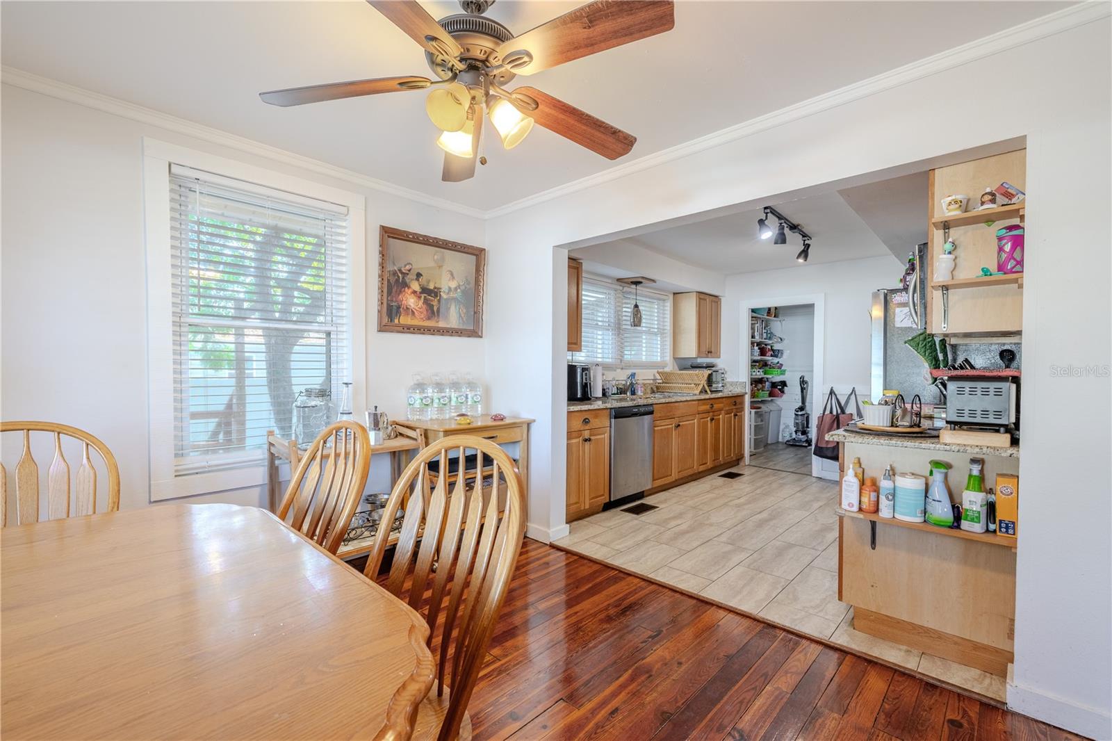 This view highlights the seamless flow from the dining room into the kitchen, creating an open and practical layout for everyday living and entertaining. The dining area features warm original wood flooring and abundant natural light, while the kitchen showcases granite countertops, wood cabinetry, and tile flooring for easy maintenance. The wide opening between the two spaces enhances connectivity and makes serving meals effortless. This functional design adds to the home’s inviting and comfortable atmosphere.