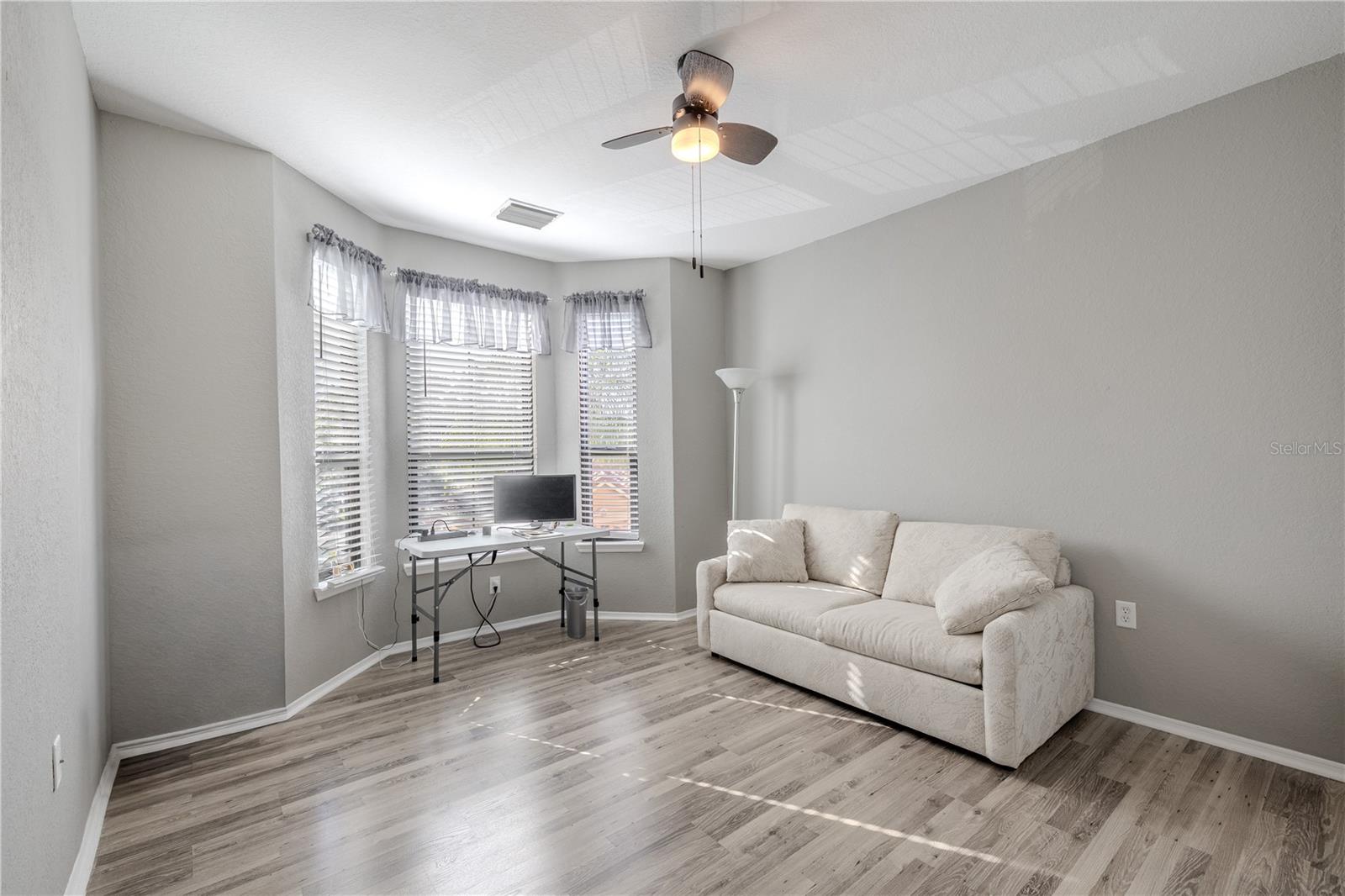 This bright second bedroom features multiple windows for natural light, neutral finishes, wood-look laminate flooring, and ample space to function comfortably as a guest room, home office, or flex space.