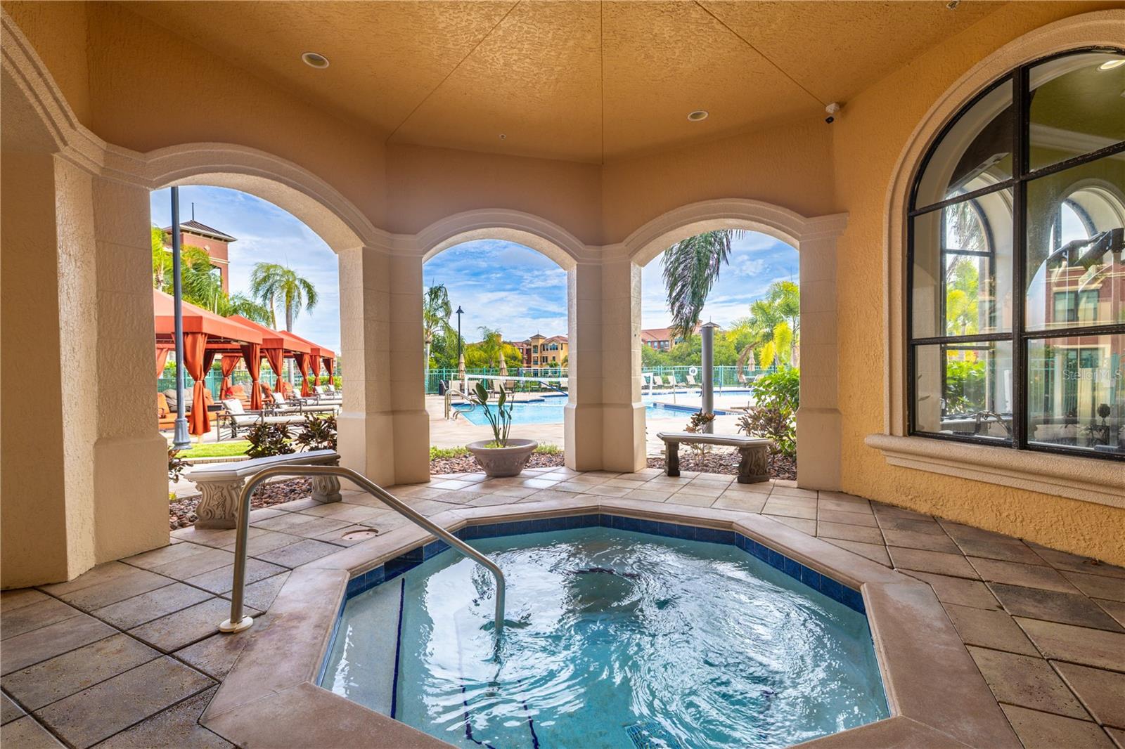 Covered heated spa area at the clubhouse featuring an inviting hot tub framed by elegant arches, with easy access to the resort-style pool deck and cabanas just beyond.