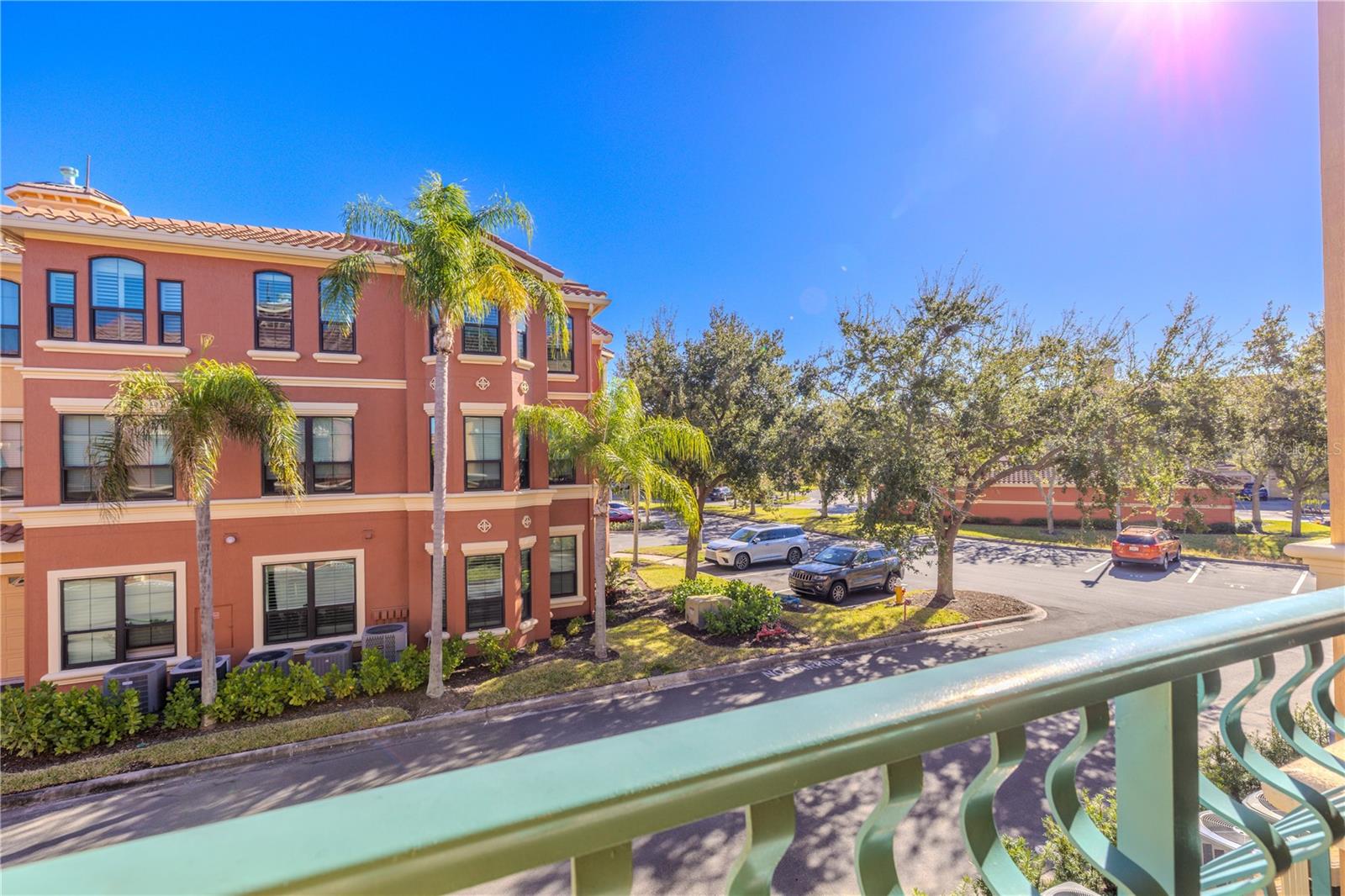 Sunny balcony view overlooking the beautifully maintained, palm-lined community with nearby parking and charming Mediterranean-style architecture.