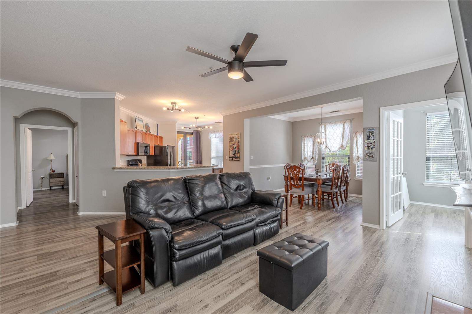 Spacious open-concept living area with updated vinyl wood-look flooring, crown molding, and a modern ceiling fan, flowing seamlessly into the dining space and kitchen for easy everyday living and entertaining.