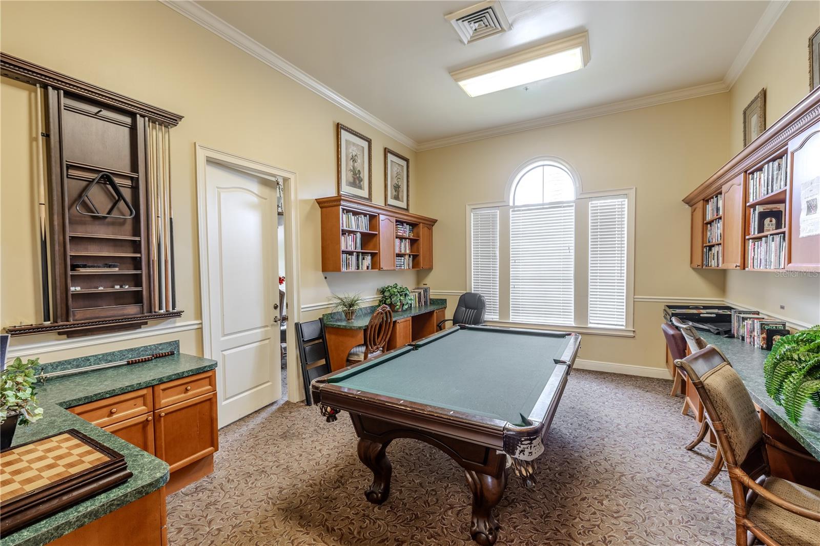 Clubhouse game and lounge room featuring a billiards table, built-in counters and cabinetry, and a bright arched window—perfect for socializing, playing pool, or relaxing with neighbors.