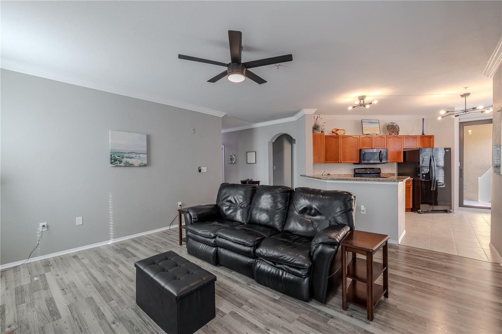 Spacious open living area with updated flooring, crown molding, and a modern ceiling fan, offering a seamless flow to the kitchen with a breakfast bar—ideal for relaxing or entertaining.