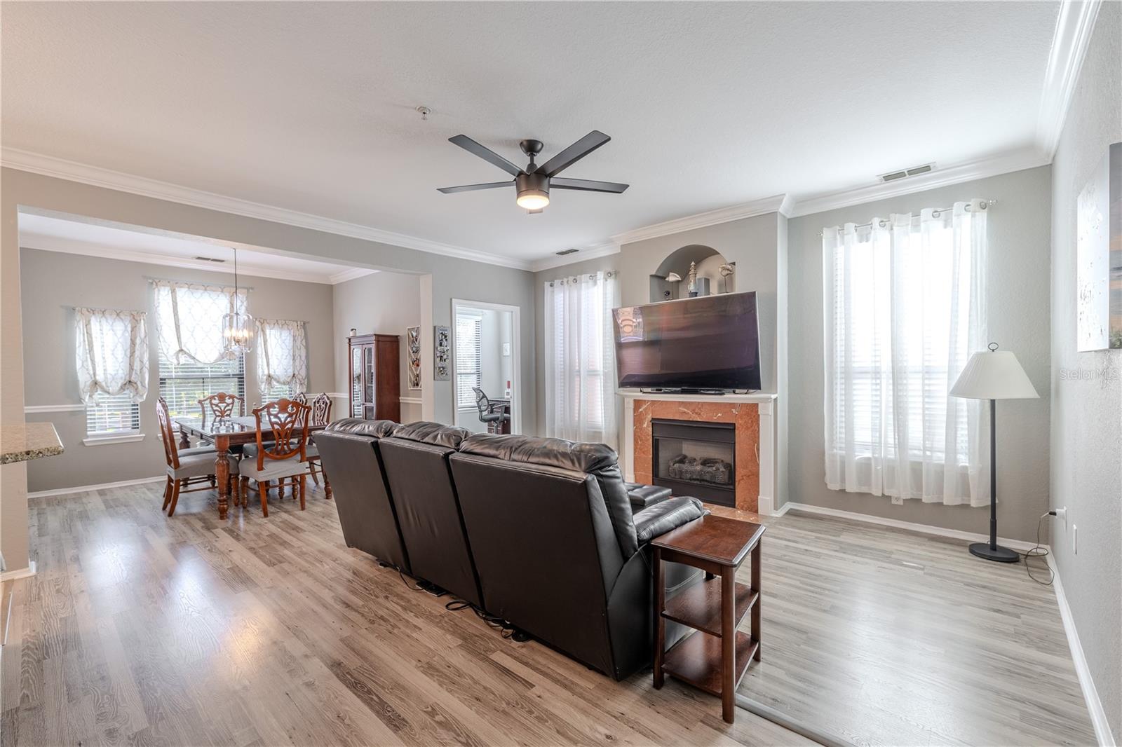 Another view of this inviting living area is anchored by a gas fireplace with a classic mantle and decorative niche above, flanked by tall windows with sheer curtains that fill the space with soft, natural light.