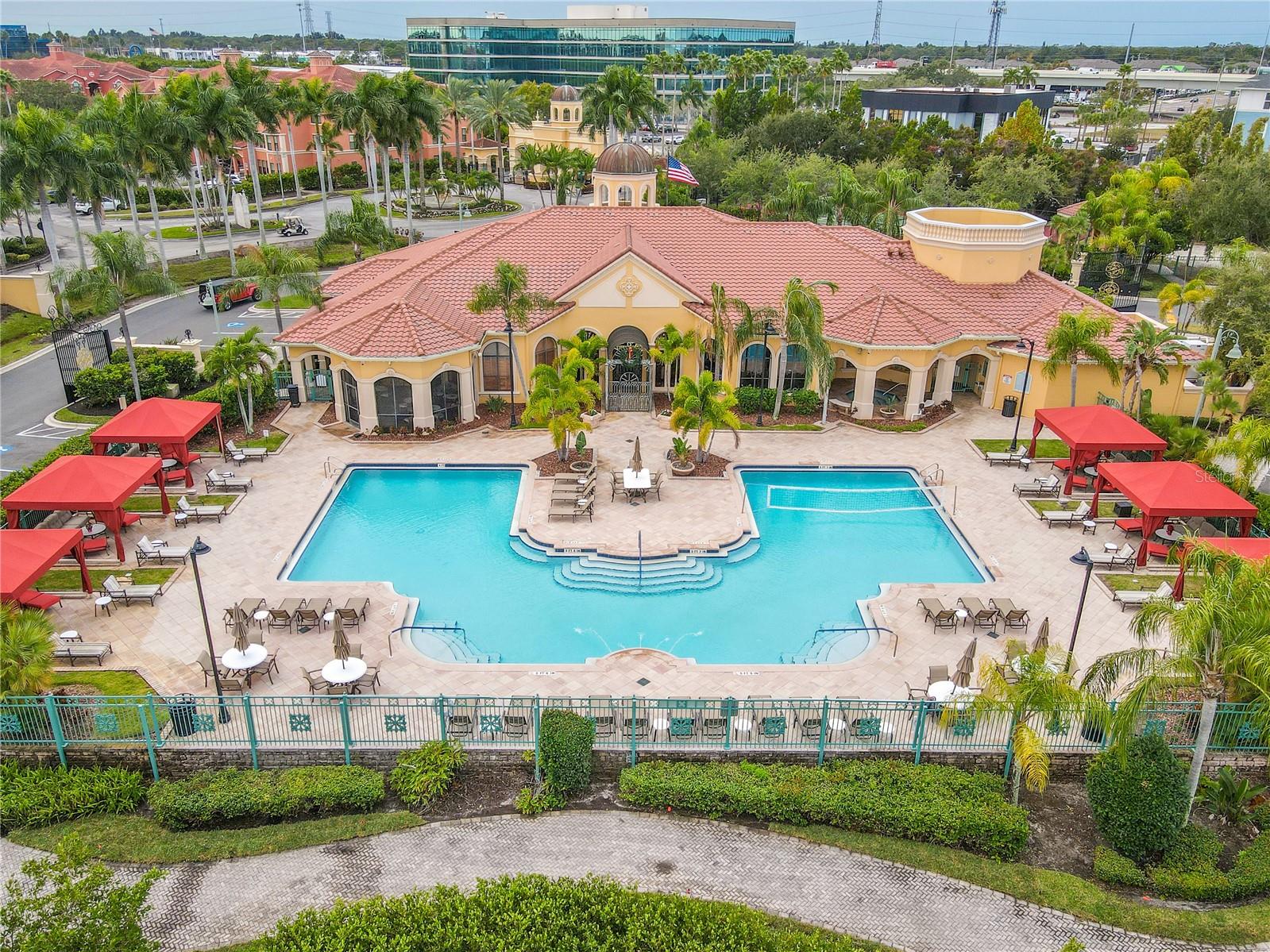 Front aerial resort-style heated clubhouse pool and spa with a spacious sundeck, lounge seating, and private rentable cabanas—perfect for relaxing, entertaining, and soaking up the Florida sunshine.