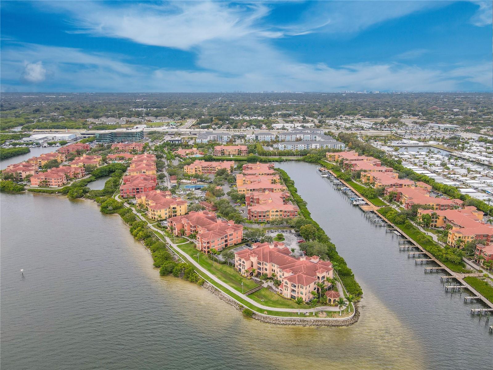 Another elevated aerial waterside view highlights the Mediterranean-style architecture of the Grand Bellagio community, showcasing tile-roofed buildings, palm-lined grounds.
