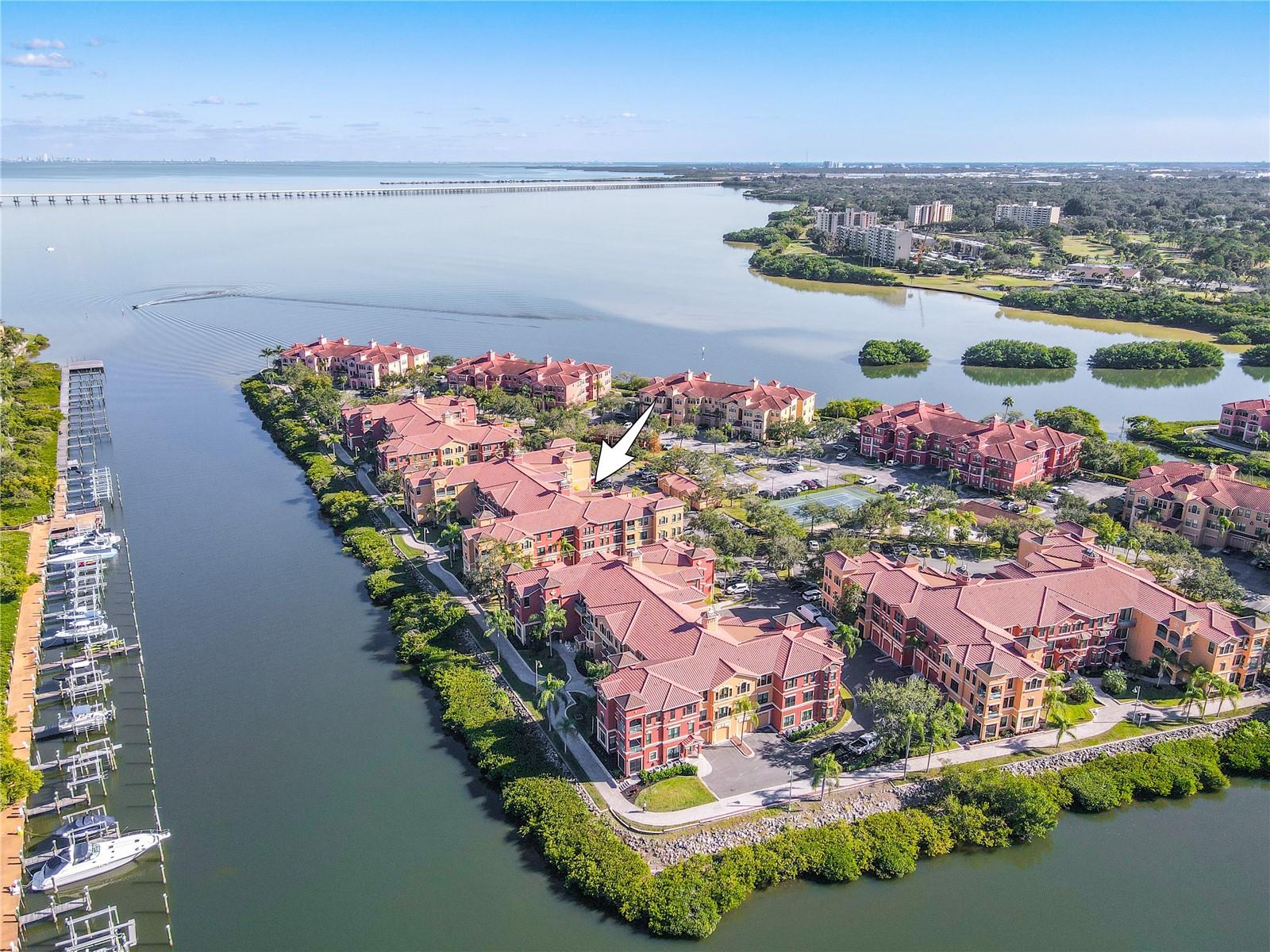 Another elevated aerial view highlights the Mediterranean-style architecture of the Grand Bellagio community, showcasing tile-roofed buildings, palm-lined grounds, and the desirable corner placement of this residence within a beautifully maintained setting.
