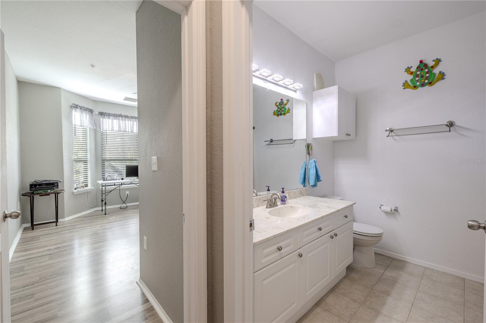 This second full bathroom offers a clean, bright design with a white vanity, solid-surface countertop, ample storage, and a convenient layout located just off the hallway and adjacent to the second bedroom.