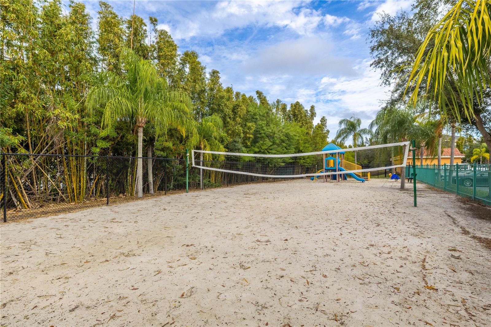 Community sand volleyball court and playground area, surrounded by lush tropical landscaping—perfect for outdoor fun and active living.