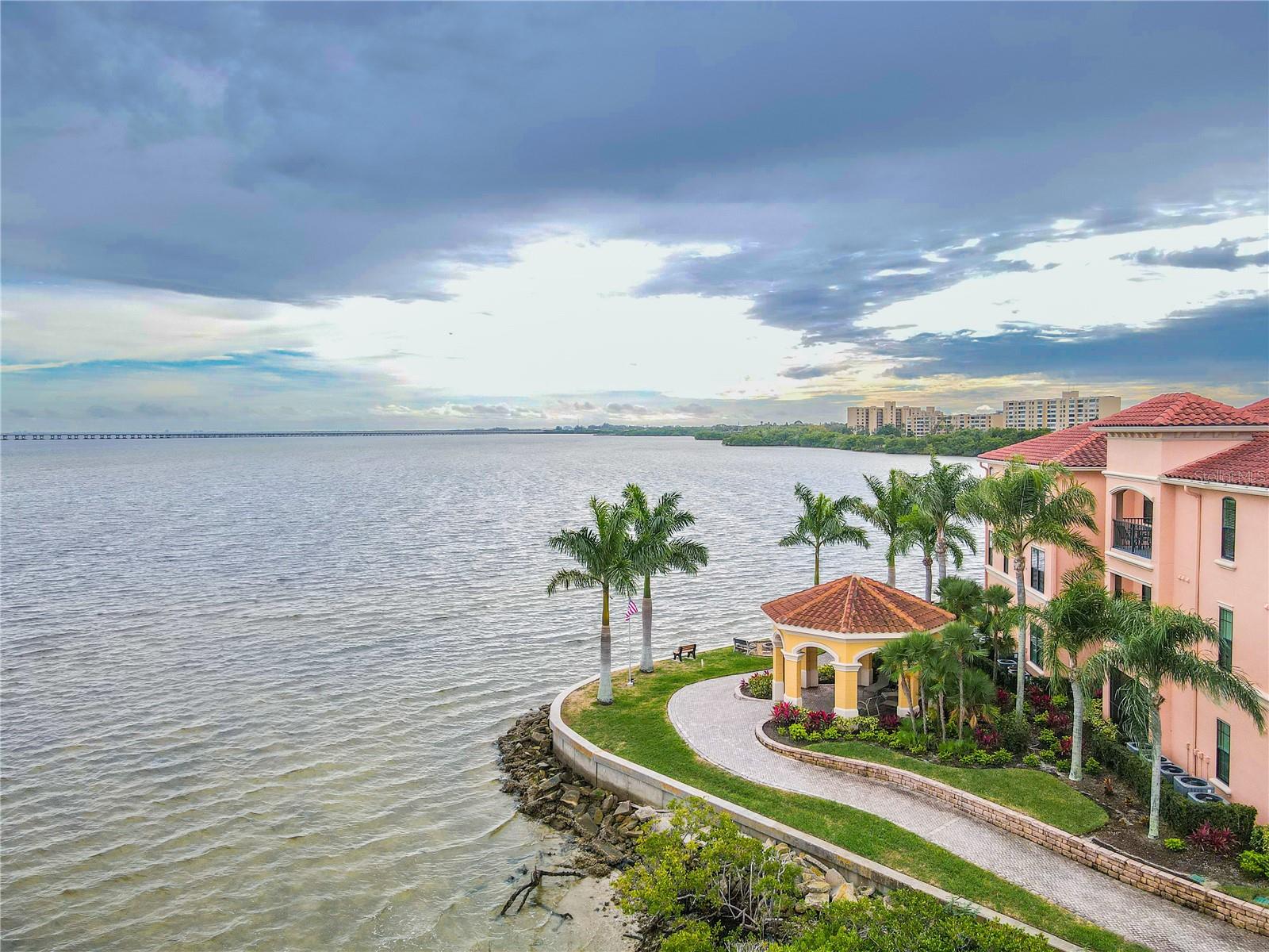 Another elevated aerial waterside view highlights the Mediterranean-style architecture of the Grand Bellagio community, showcasing tile-roofed buildings, palm-lined grounds.