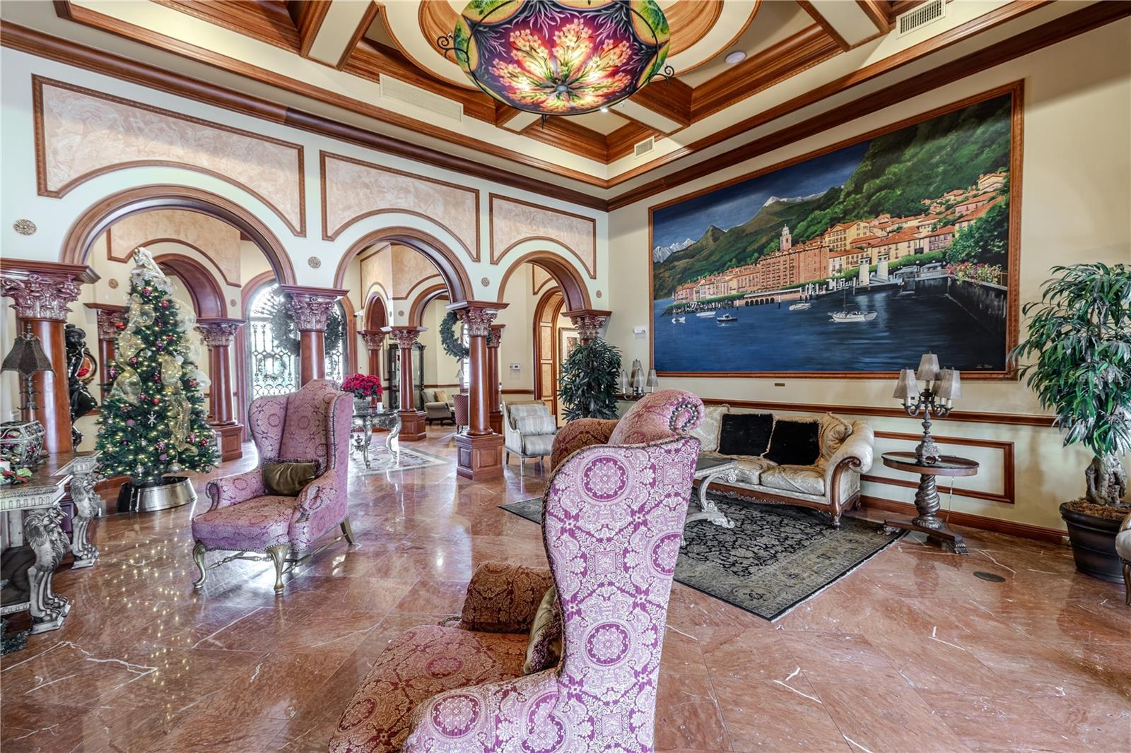 Another view of the grand clubhouse lounge with soaring coffered ceilings, dramatic murals and arched columns, gleaming marble floors, and an elegant fireplace seating area that creates a truly resort-style welcome.