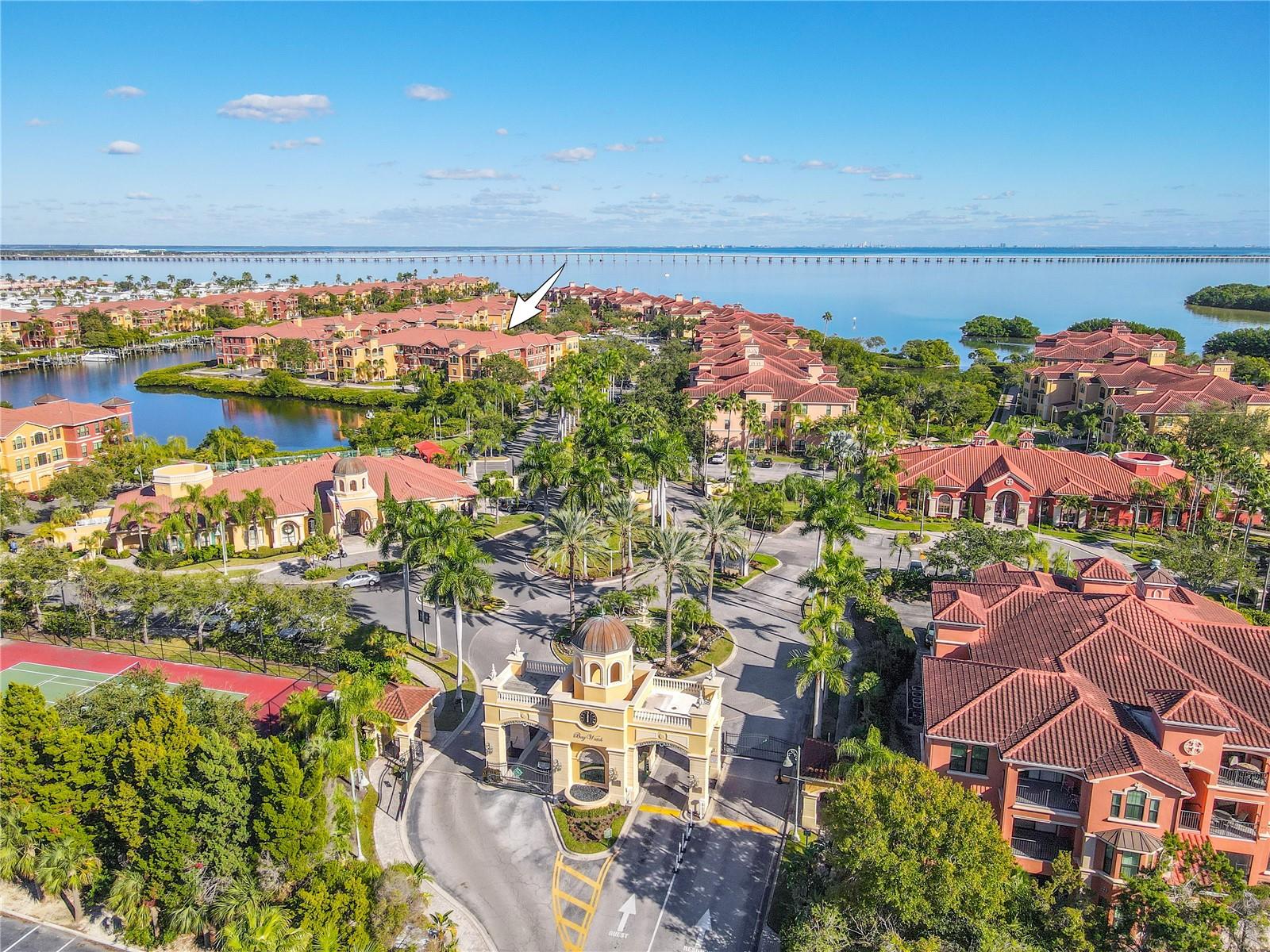 An elevated aerial view highlights the Mediterranean-style architecture of the Grand Bellagio community, showcasing tile-roofed buildings, palm-lined grounds, and the desirable corner placement of this residence within a beautifully maintained setting.