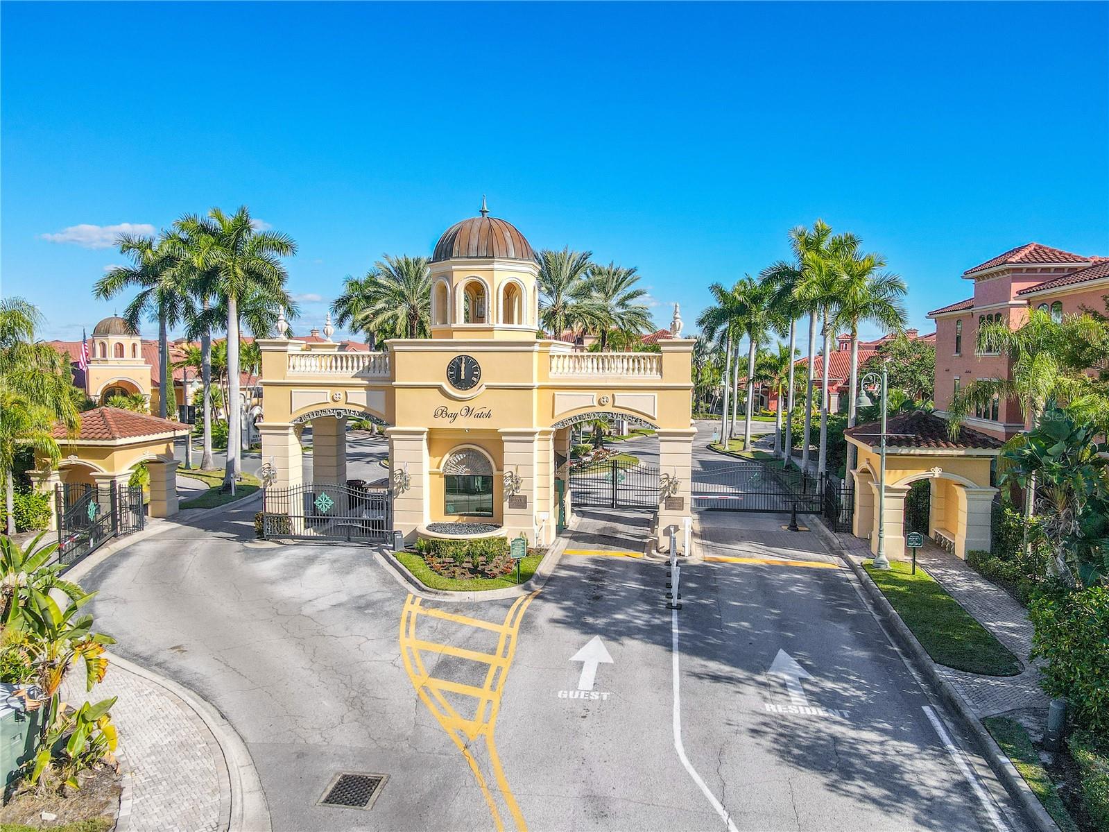 Impressive gated entrance to the Grand Bellagio condo community, featuring a grand clock-tower entry, lush palm-lined landscaping, and a beautifully maintained, resort-style community setting.