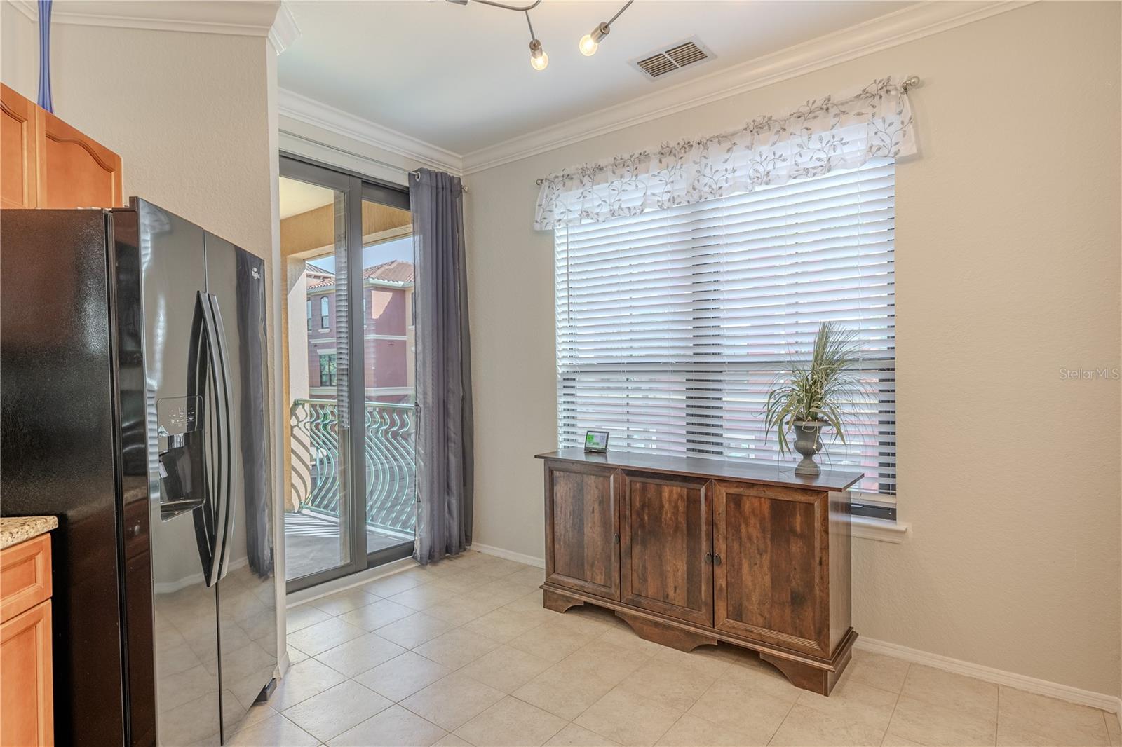 Natural light fills this eat-in kitchen area, featuring a large window, tile flooring, modern lighting, and sliding glass doors that open to the private balcony for easy indoor–outdoor living.