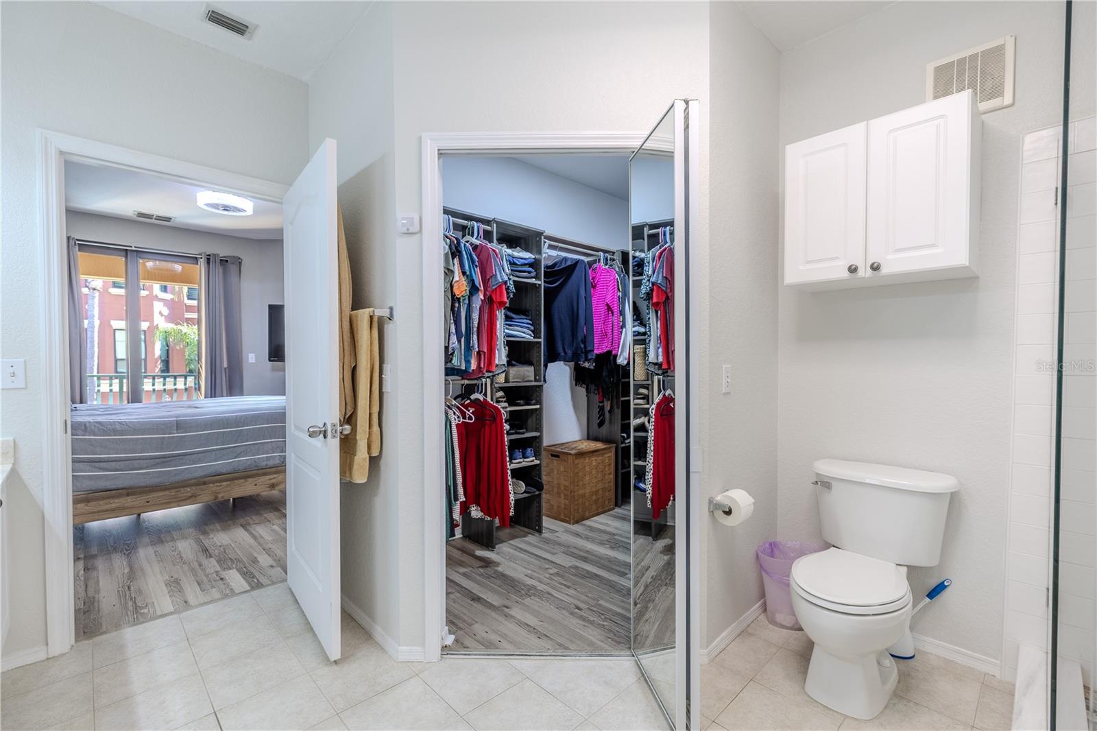 Primary bath area with a walk-in closet, private water closet, and a glass-enclosed shower, with easy access back to the bedroom and balcony beyond.