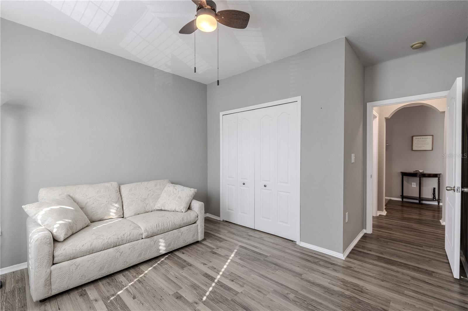 This view of the bright second bedroom features multiple windows for natural light, neutral finishes, wood-look laminate flooring, built in closet, and ample space to function comfortably as a guest room, home office, or flex space.