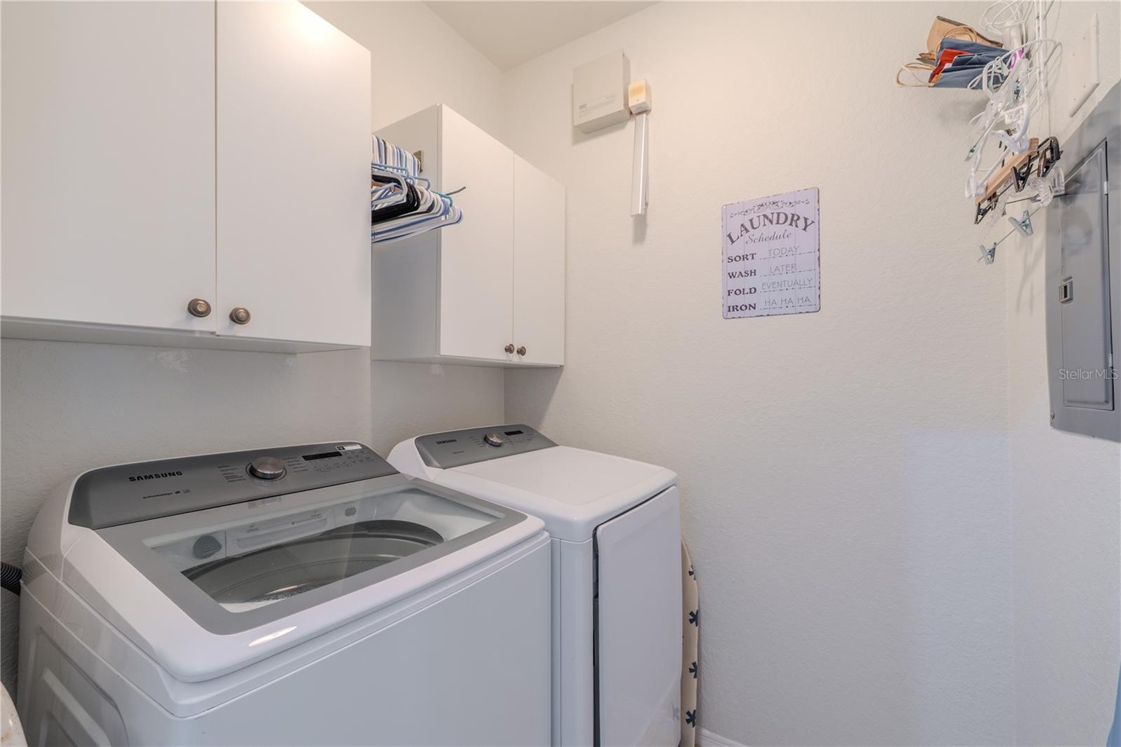 This dedicated interior laundry closet features a full-size washer and dryer, overhead cabinetry for storage, hanging space, and convenient access to the electrical panel, making everyday chores efficient and well organized.