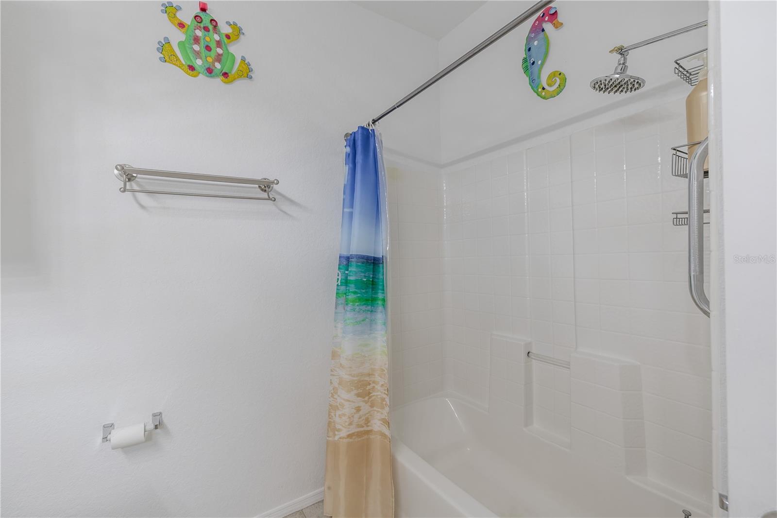 This clean and well-appointed tub/shower combination features crisp white tile surround, built-in shelving, updated fixtures, and a bright, beach-inspired aesthetic that complements the home’s coastal feel.