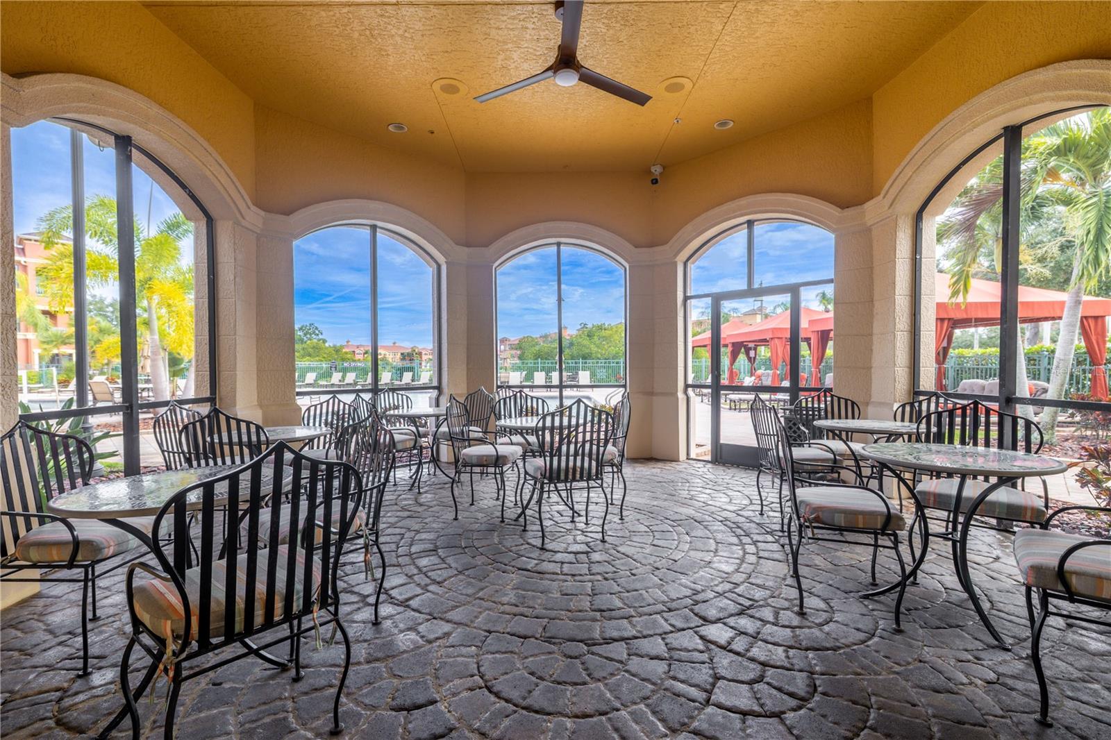 Covered poolside pavilion with café-style seating, ceiling fan, and charming arched openings—perfect for relaxing in the shade while enjoying views of the resort-style pool and cabanas.