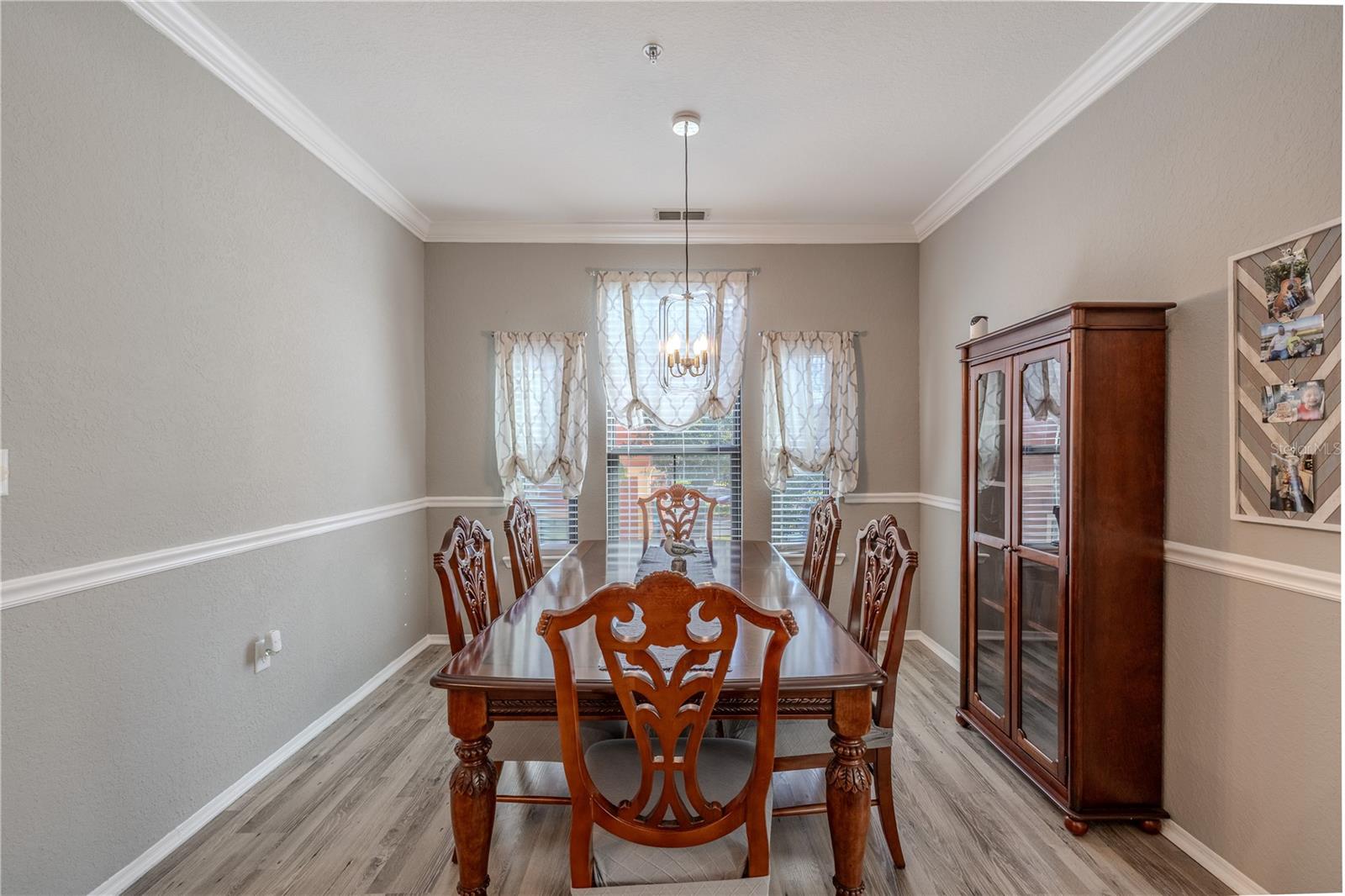 An elegant dining room features crown molding, chair rail detailing, wide-plank laminate flooring, and a modern pendant light, creating a refined space perfect for hosting gatherings and formal meals.