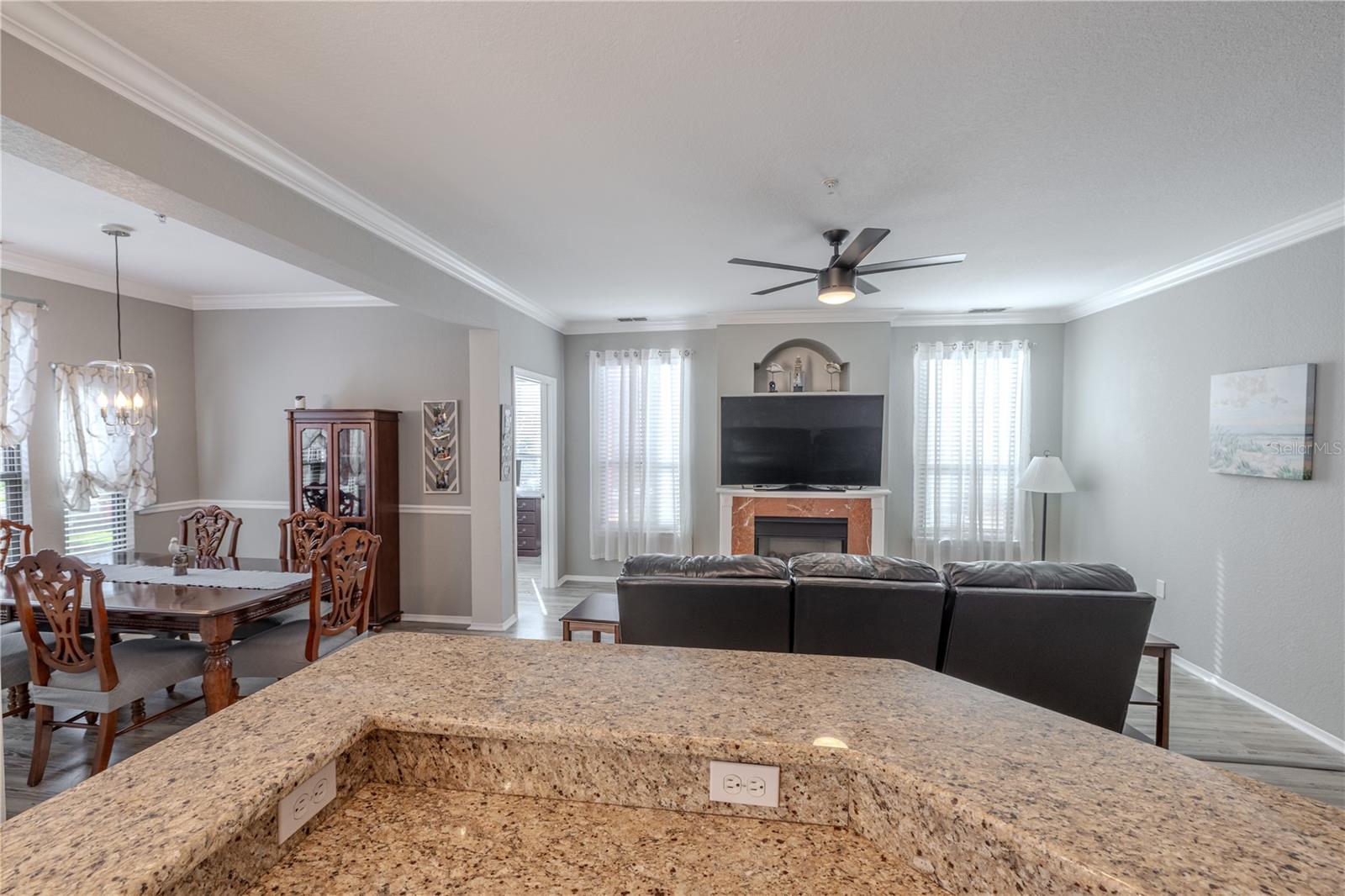 From the kitchen, the expansive granite counter overlooks the living and dining areas, highlighting the open layout, abundant natural light, and a cozy living room centered around a fireplace and modern ceiling fan.