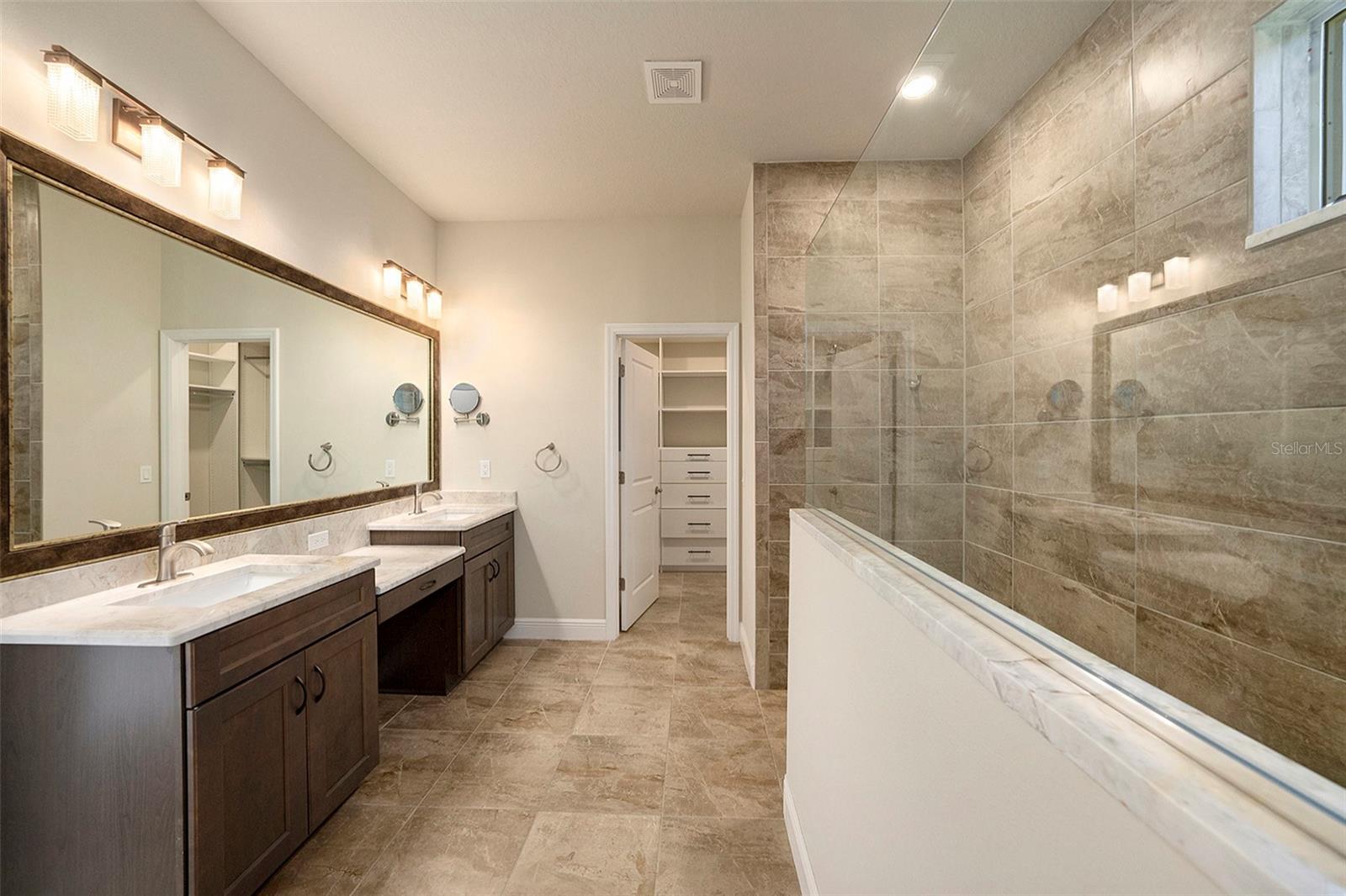 Primary bathroom with double vanities and large walk in shower and 2 walk in closets