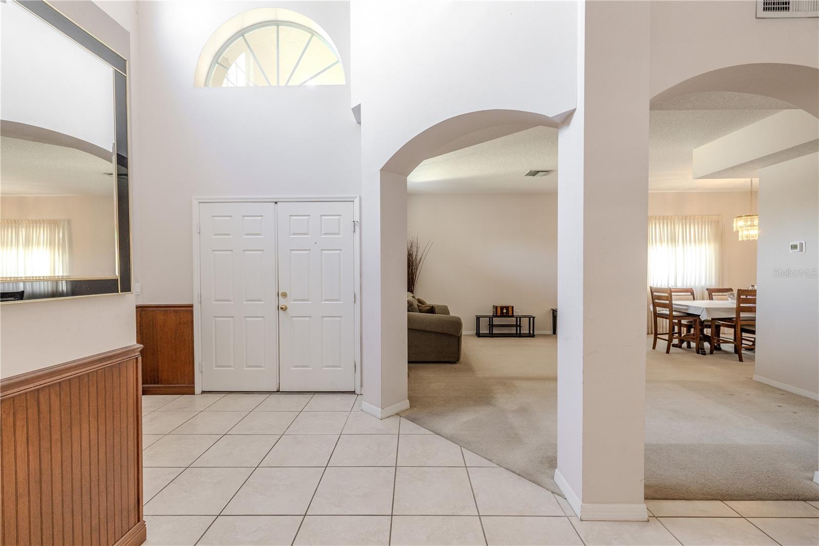 Inviting two-story foyer, tiled entryway with soaring ceilings, wood wainscoting panels, arched openings, and a bright transom window that fills the home with natural light and an airy, open feel.