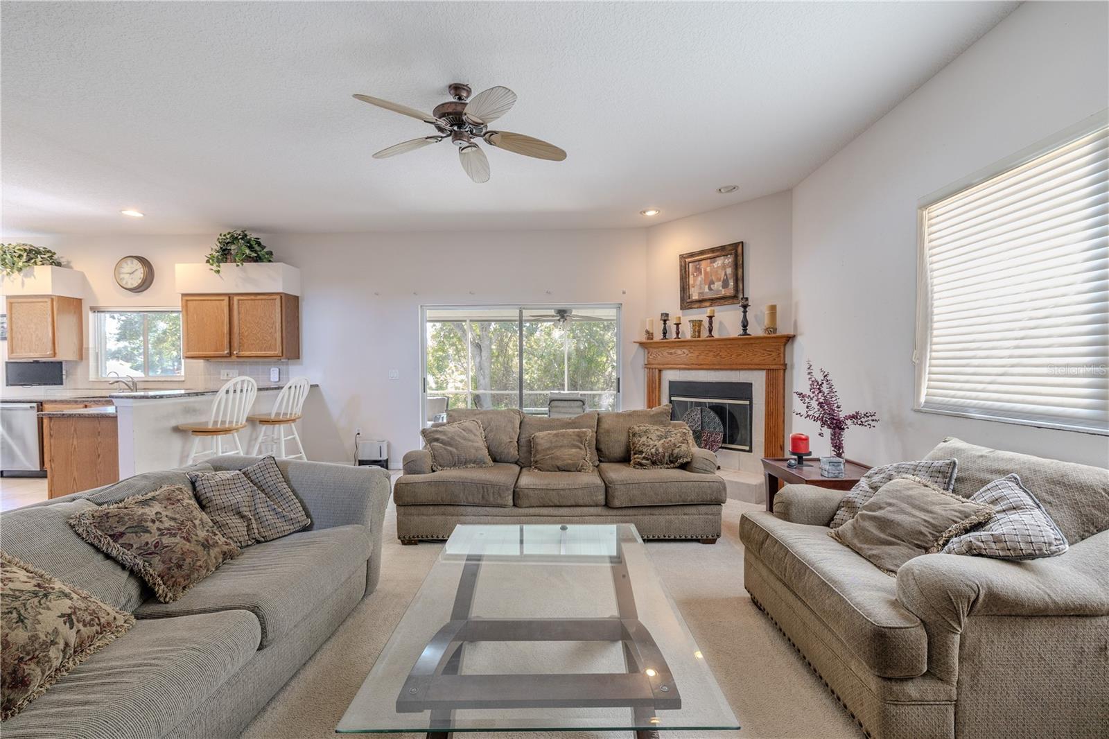 Spacious family room features a cozy fireplace, ceiling fan, and sliding doors to the screened lanai, with an open flow to the kitchen and breakfast bar for easy entertaining.