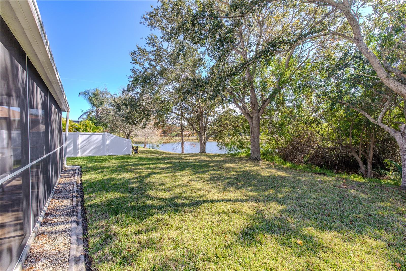 Private backyard retreat features a wide grassy lawn, mature shade trees, and tranquil pond views beyond the fully screened lanai.