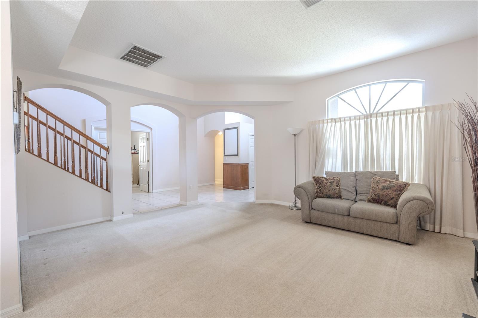 Additional view of the open-concept living and dining area featuring arched entry ways, 10 ft. ceilings, neutral carpeting, plenty of natural light, and a comfortable layout ideal for everyday living and entertaining.