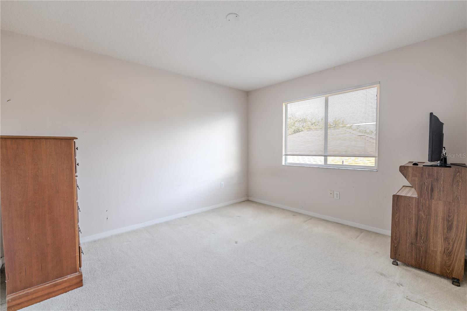Spacious fourth bedroom features plush carpeting and a large window for natural light, offering flexible space for guests, a home office, or a playroom.