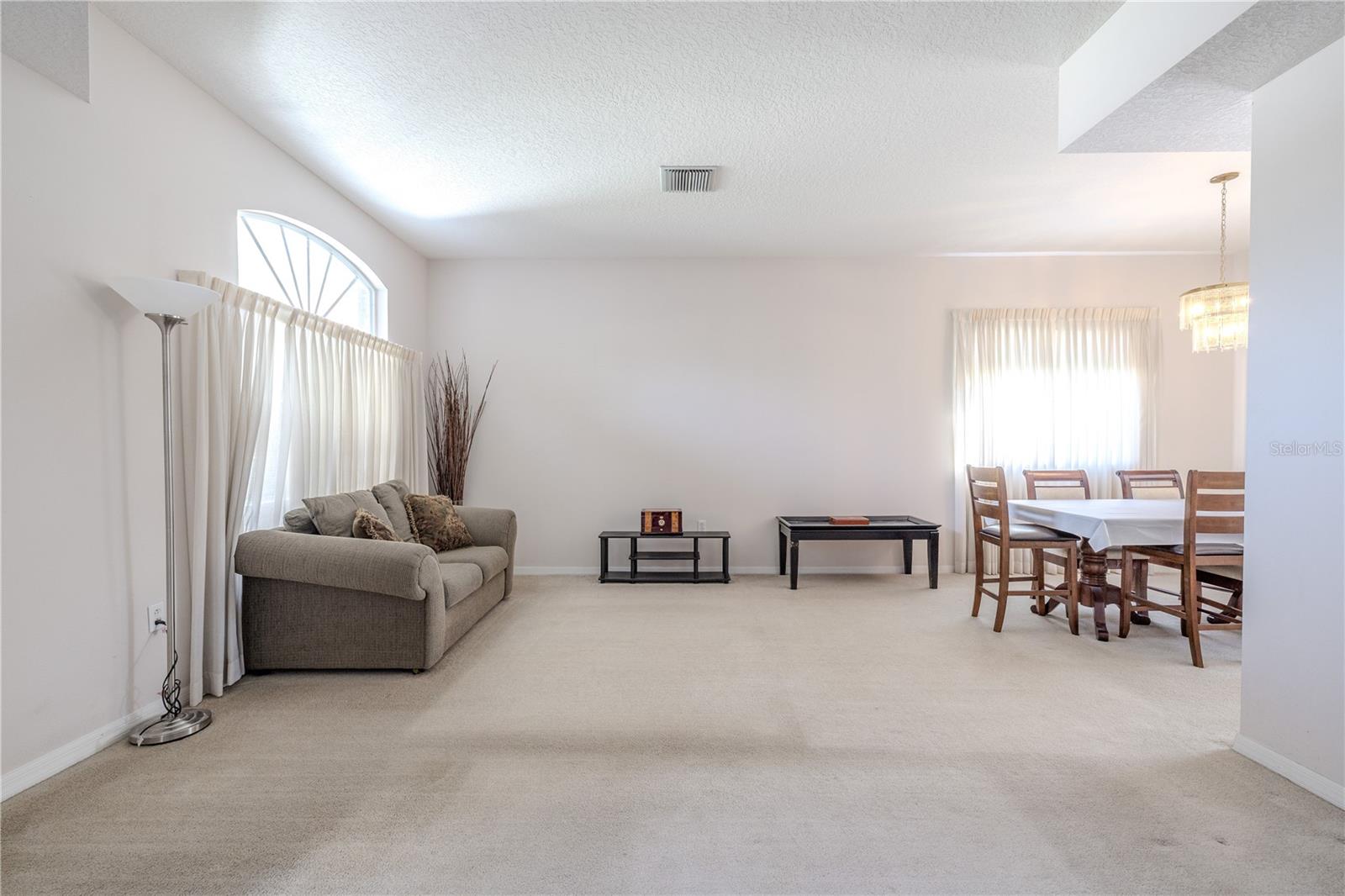 Bright, open-concept living and dining area featuring 10 ft. ceilings, neutral carpeting, plenty of natural light, and a comfortable layout ideal for everyday living and entertaining.