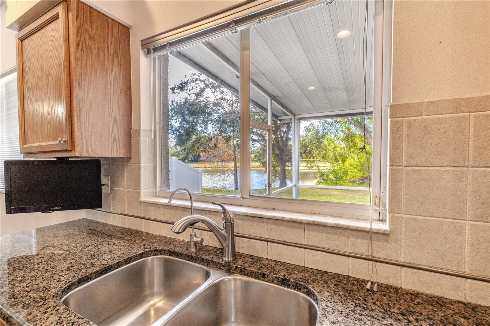 Kitchen sink window frames peaceful views of the screened lanai, mature trees, and sparkling pond beyond, bringing the outdoors in while you cook and clean.