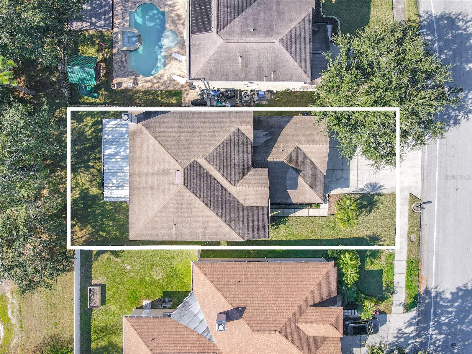 Aerial view showcasing the home’s generous lot with a wide front yard, long driveway, screened lanai, and ample backyard green space bordered by mature trees.