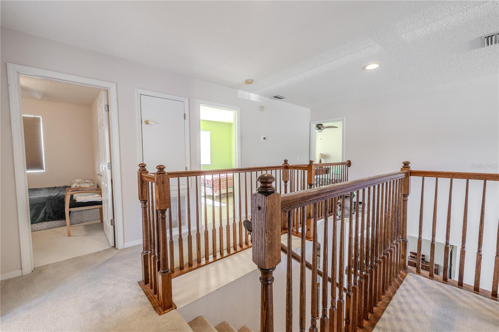 Upstairs hallway/landing features warm wood railings and a bright open feel, providing easy access to the primary and secondary bedrooms and full bath.